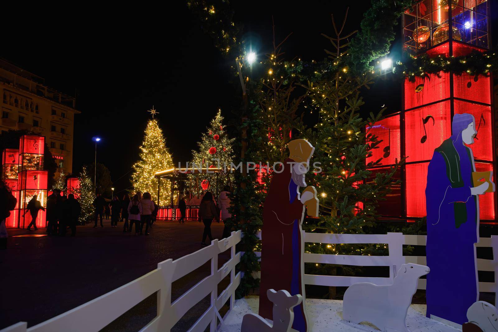 Night view of nativity scene figures with people around illuminated festive instalments at main city square.