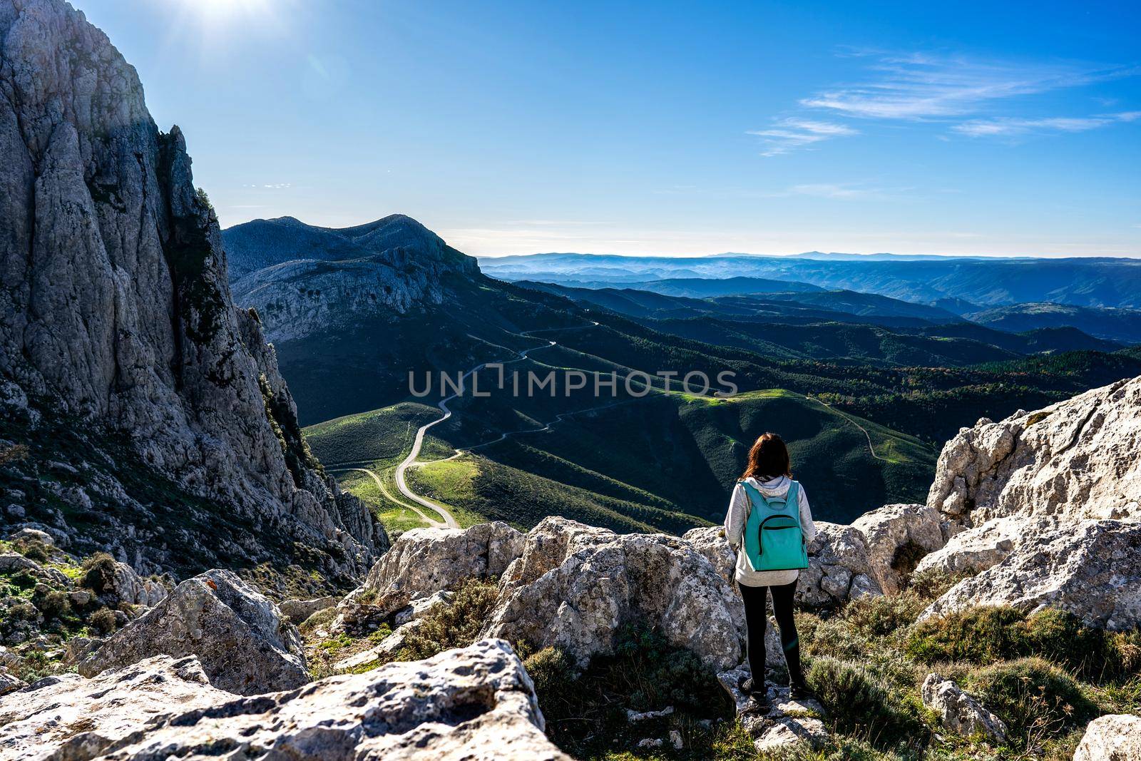 Rear view of unrecognizable carefree young woman on a mountain peak with backpack on shoulders looking to the gorgeous panorama - Solo female traveler enjoying her trip destination living nature by robbyfontanesi