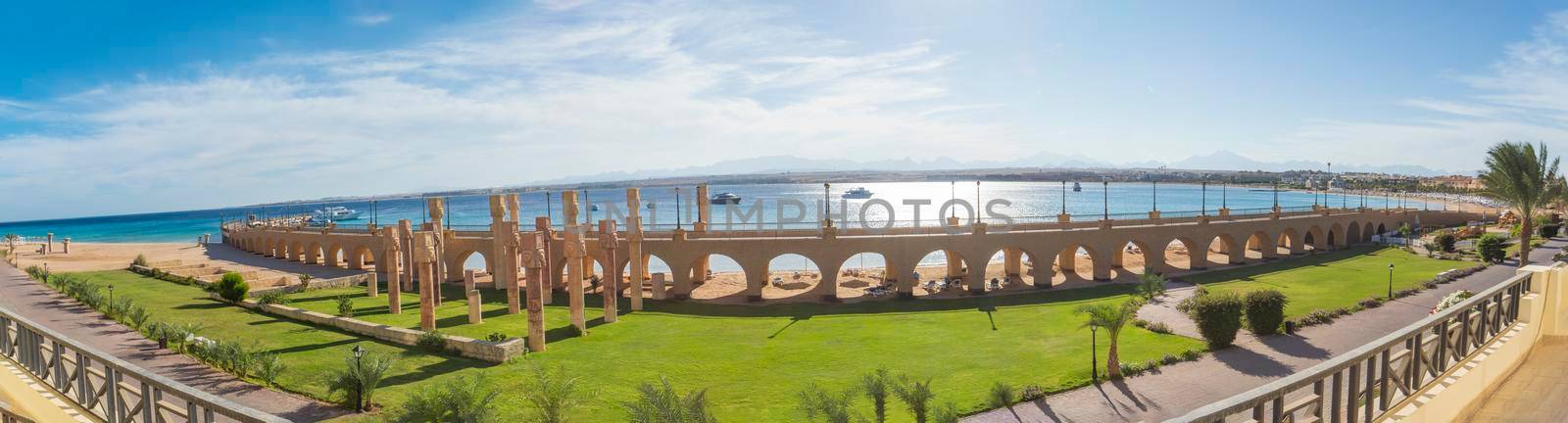View across a beautiful landscaped garden to the sea in tropical resort with large bridge and archways on beach
