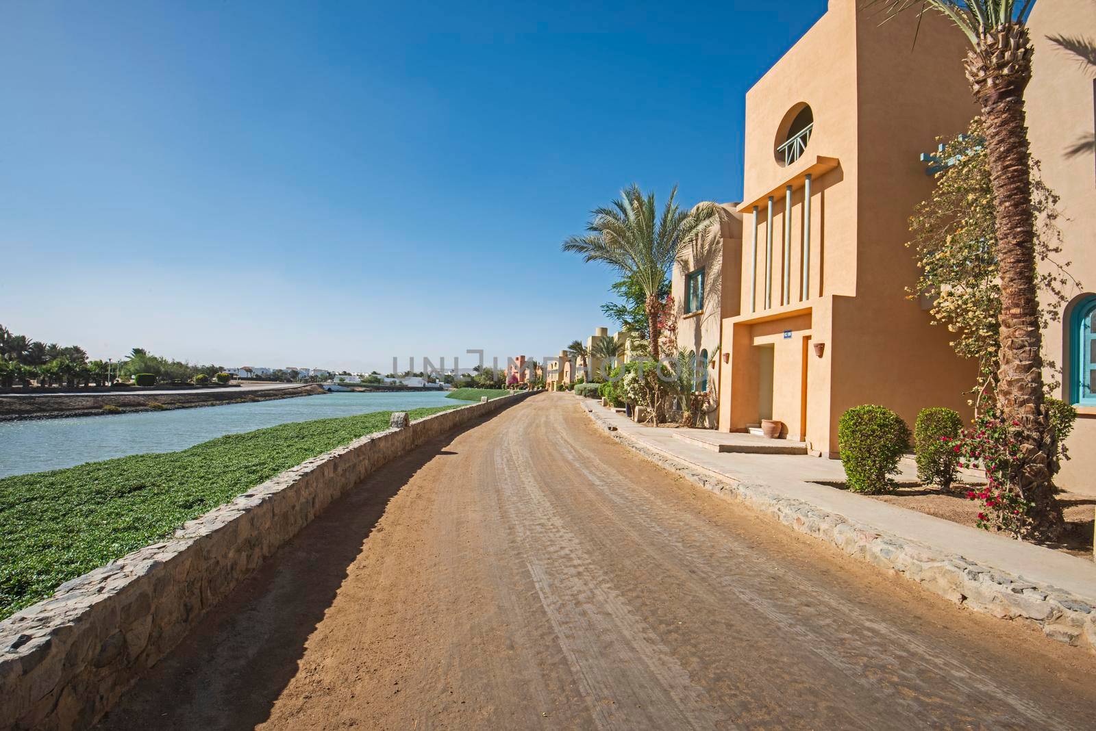 View along a sandy dirt road through beautiful landscaped gardens in tropical hotel resort with river