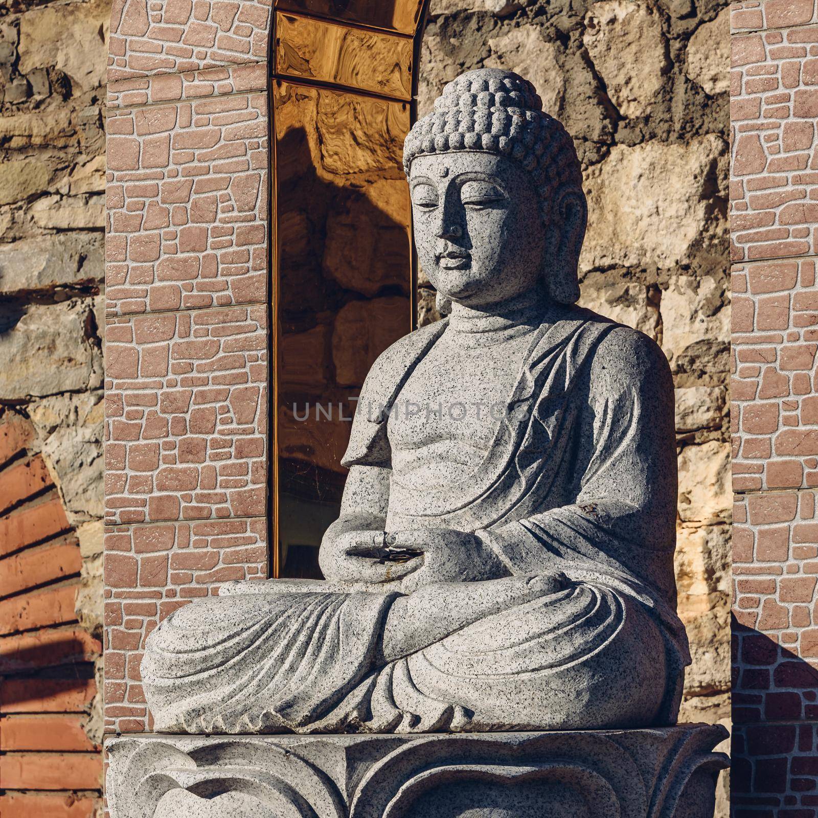 White stone statue of a Buddha on masonry background