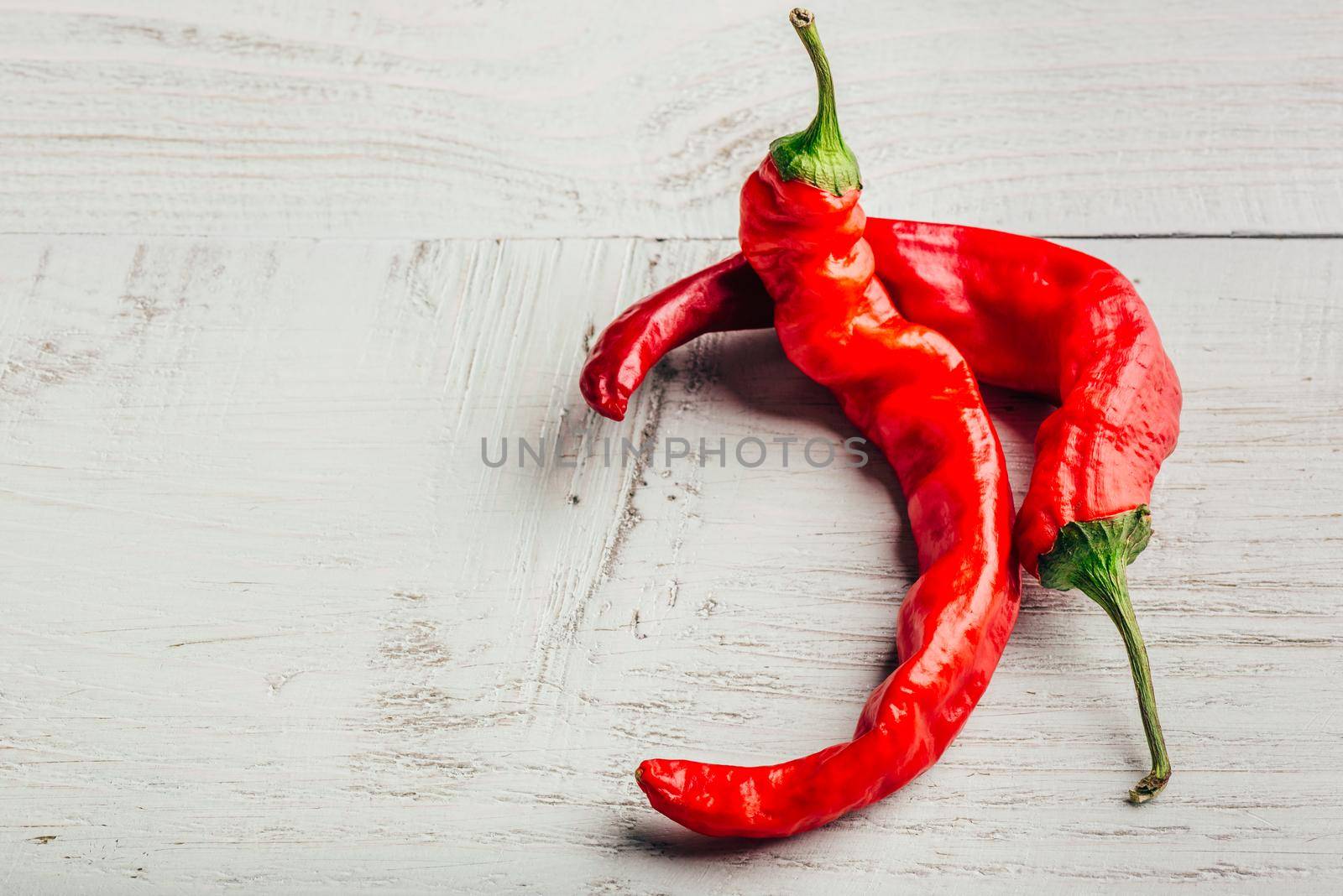 Ripe and red chili peppers over light wooden background.