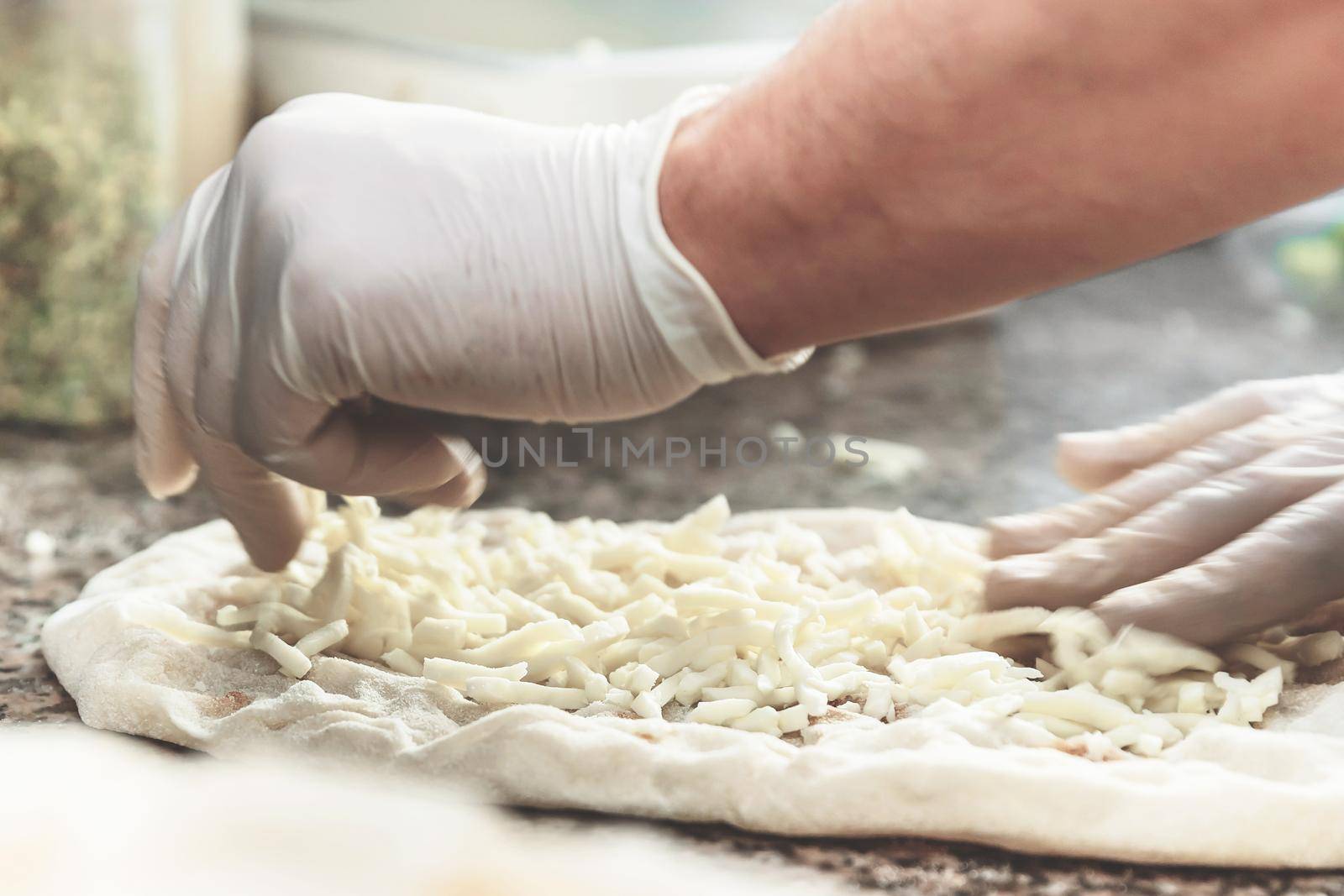 Hands with plastic gloves of pizza chef making pizza at kitchen