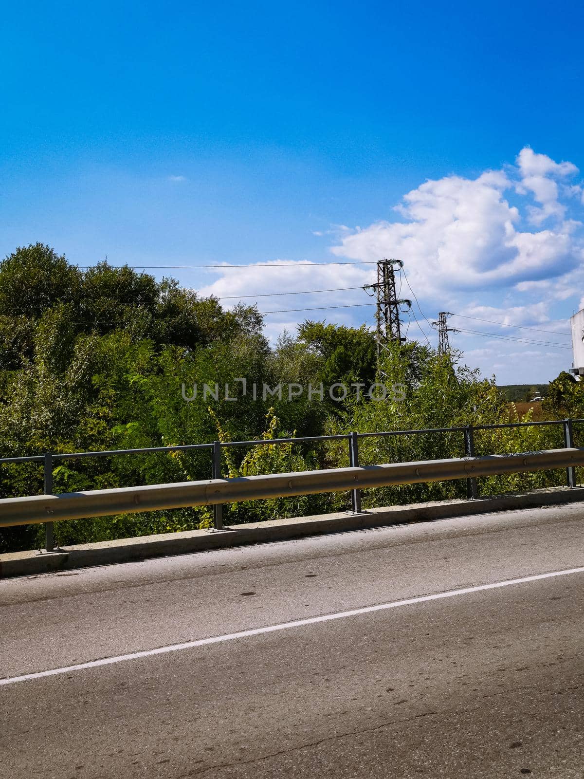 Vertical shot of power lines under a cloudy sky by the roadside