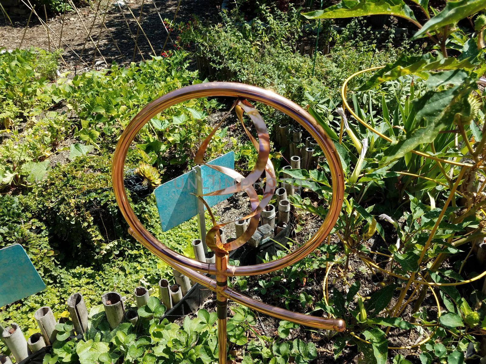 circular copper metal fountain in garden with plants and flowers