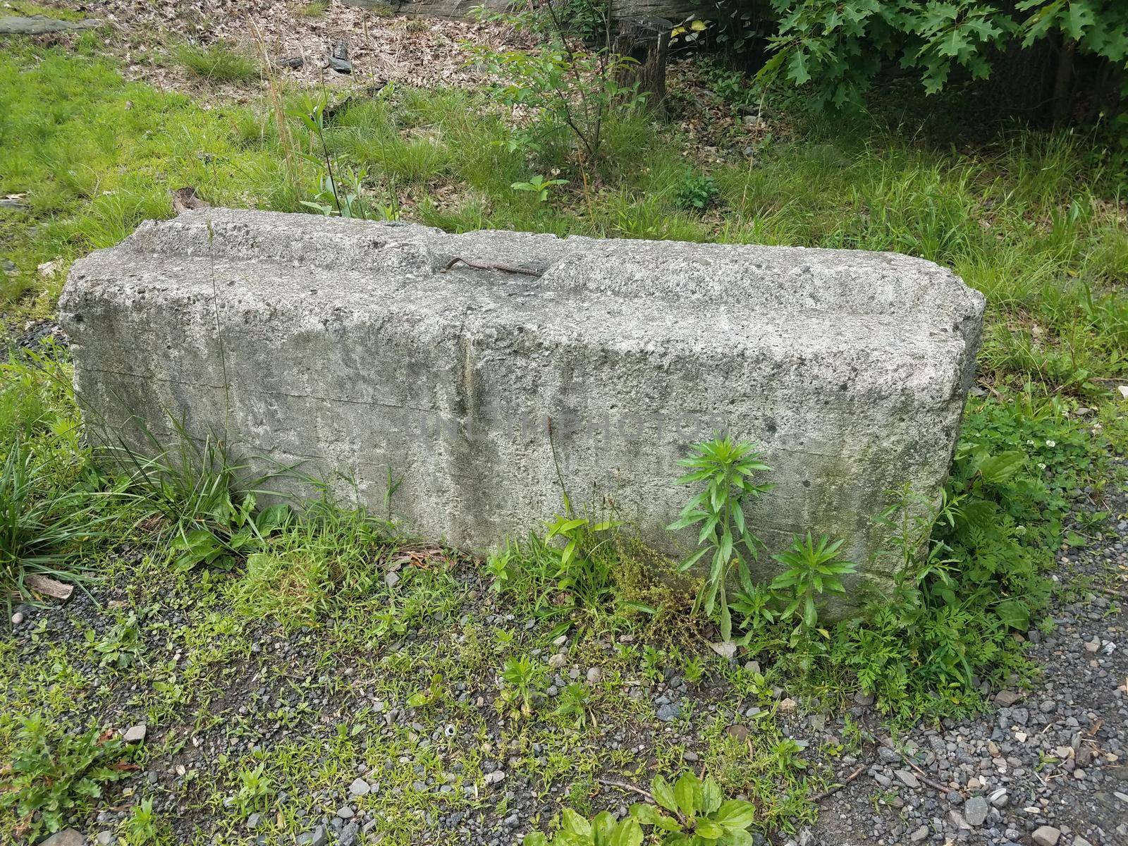 large or heavy grey cement barricade with pebbles and green grass