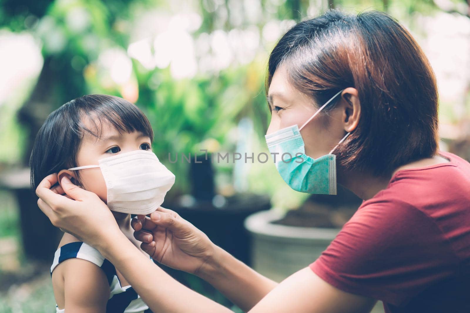 Mother take care daughter with face mask for protection disease flu or covid-19 outdoors, mom wearing on medical mask with child safety for protect outbreak of pandemic, medical concept. by nnudoo