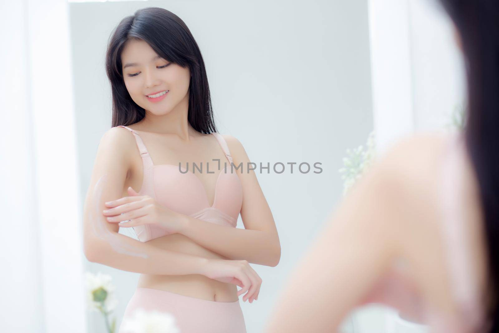 Beautiful sexy young asian woman looking mirror applying cream on arms and message, beauty girl applying body lotion skin care for health and soft hydration, treatment and cosmetic with moisturizer.