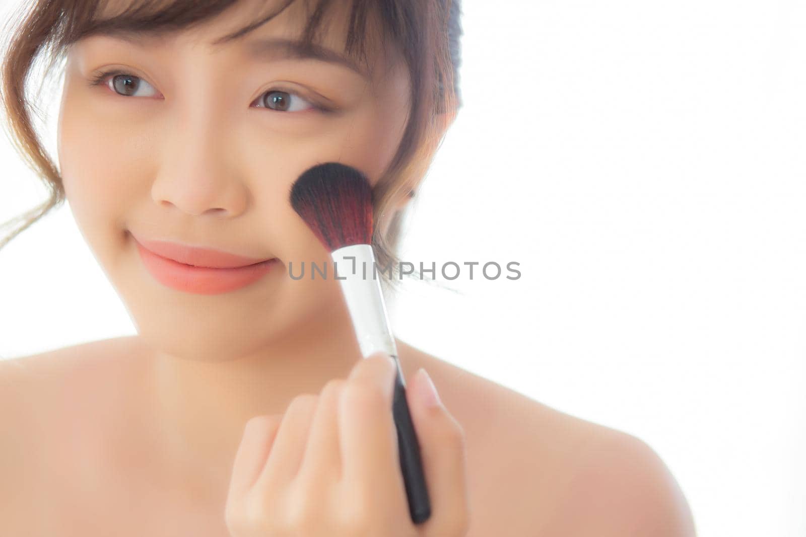 Beauty portrait young asian woman smile with face looking mirror applying makeup with brush cheek in the bedroom, beautiful of girl holding blusher, skin care and cosmetic concept.