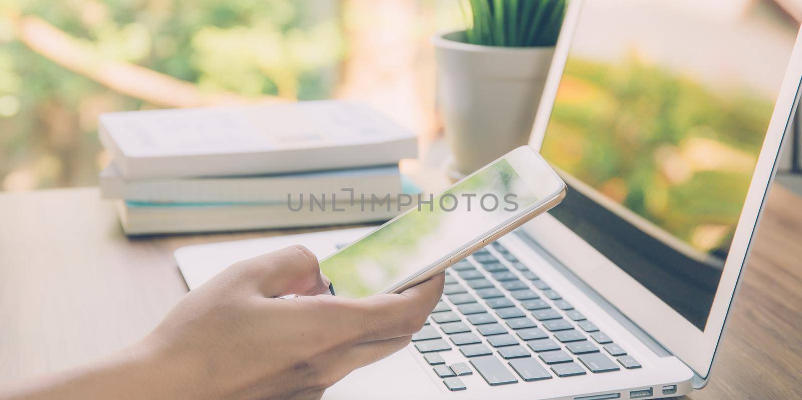 Hand of business man working from home using laptop computer on desk, lifestyle of new normal, social distancing, freelance work in stay home and look phone, communication concept, banner website. by nnudoo