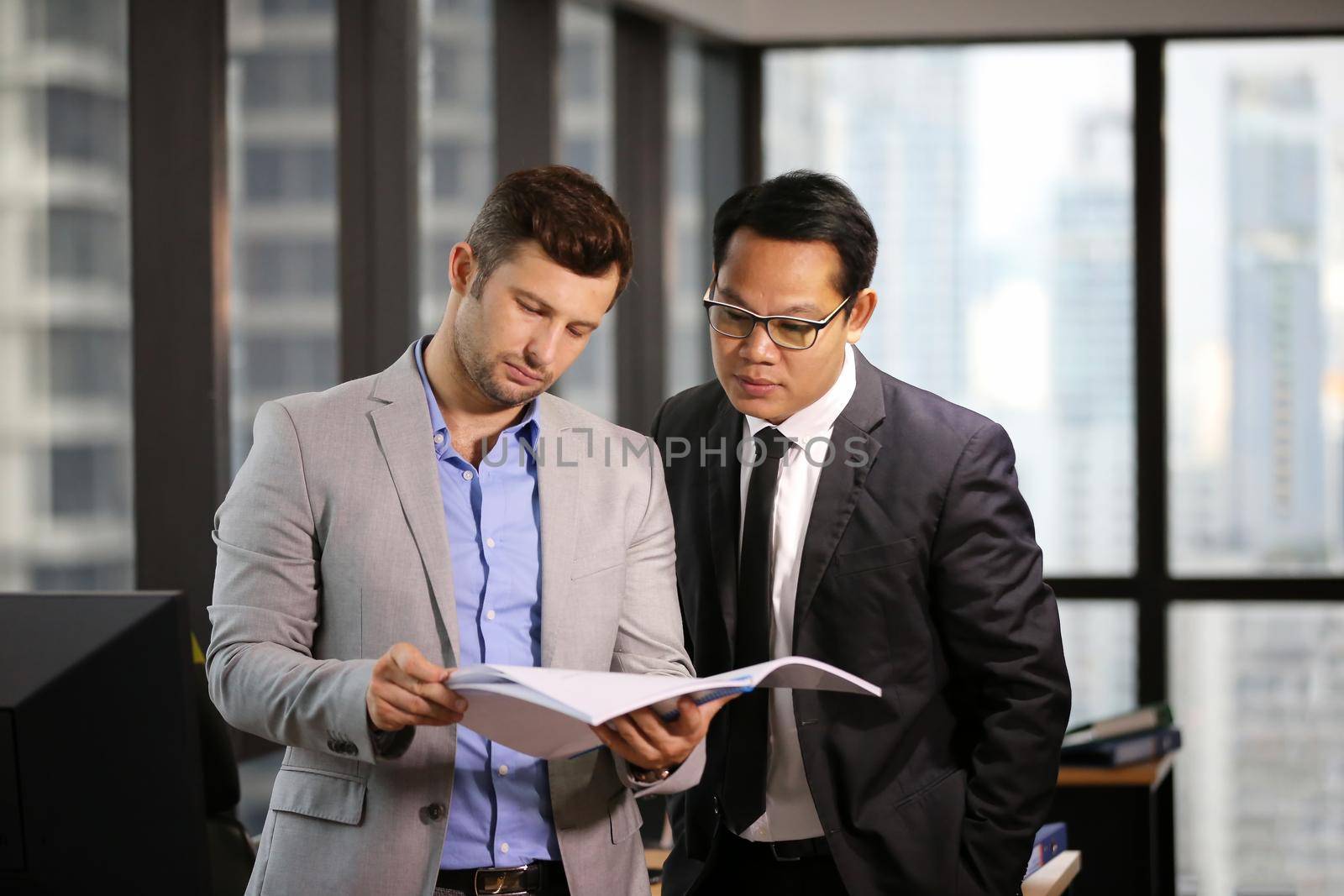 Two business colleagues working together on new project in modern office. by chuanchai