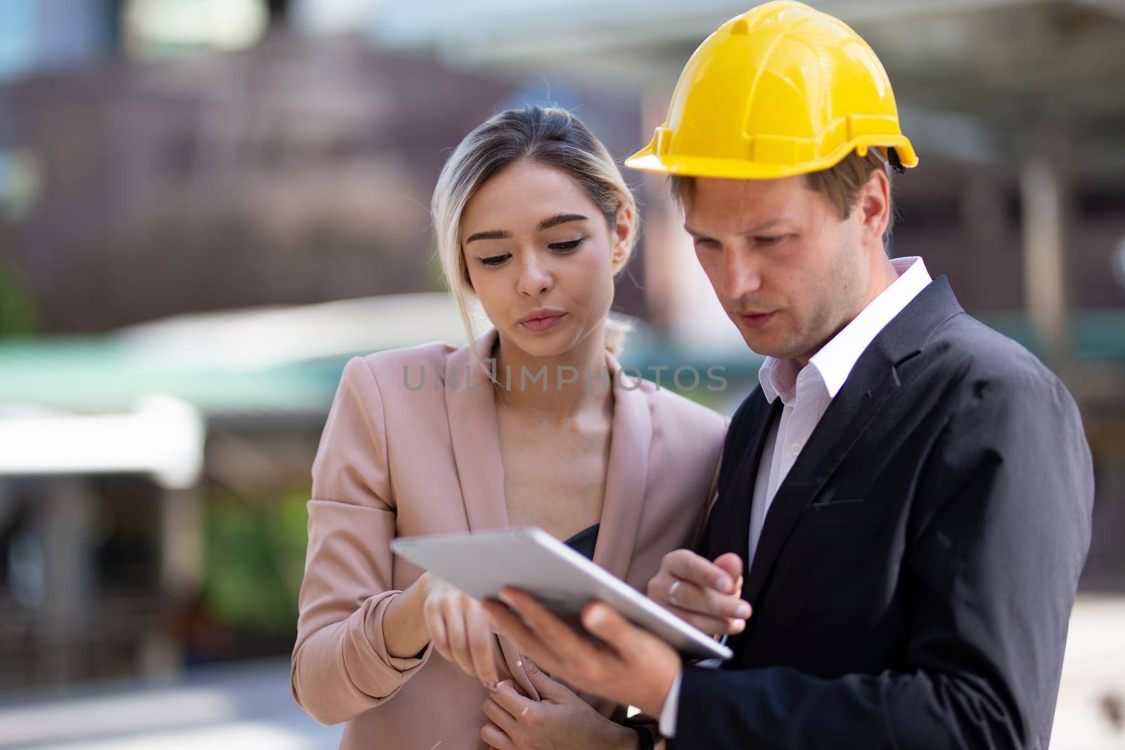 Female industrial engineer wearing a white helmet while standing in a construction site with businessman talking on working plan, Engineer and architects at construction site concept by chuanchai