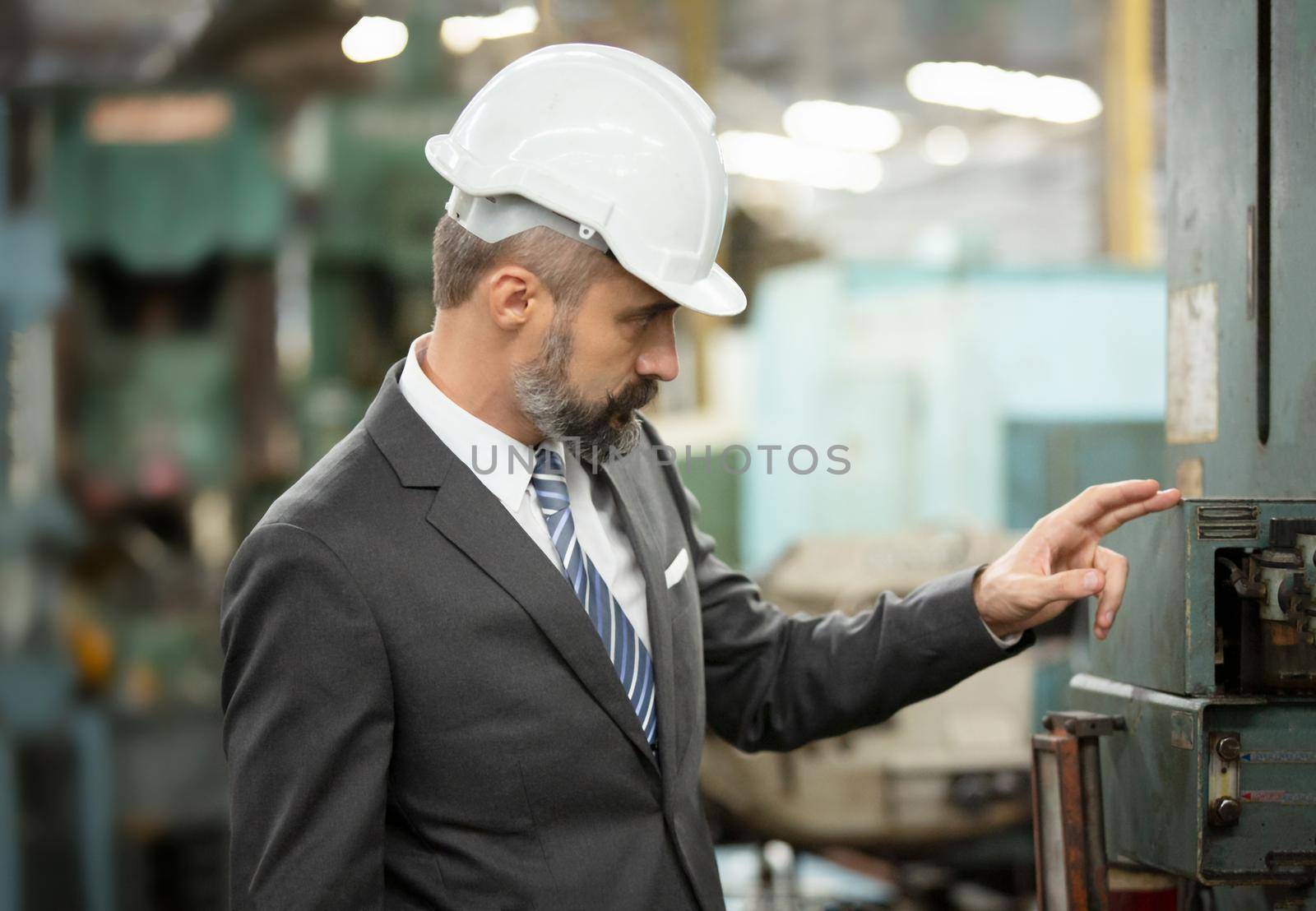 The bearded hipster director with engineer hat standing against cnc machine in production in factory by chuanchai