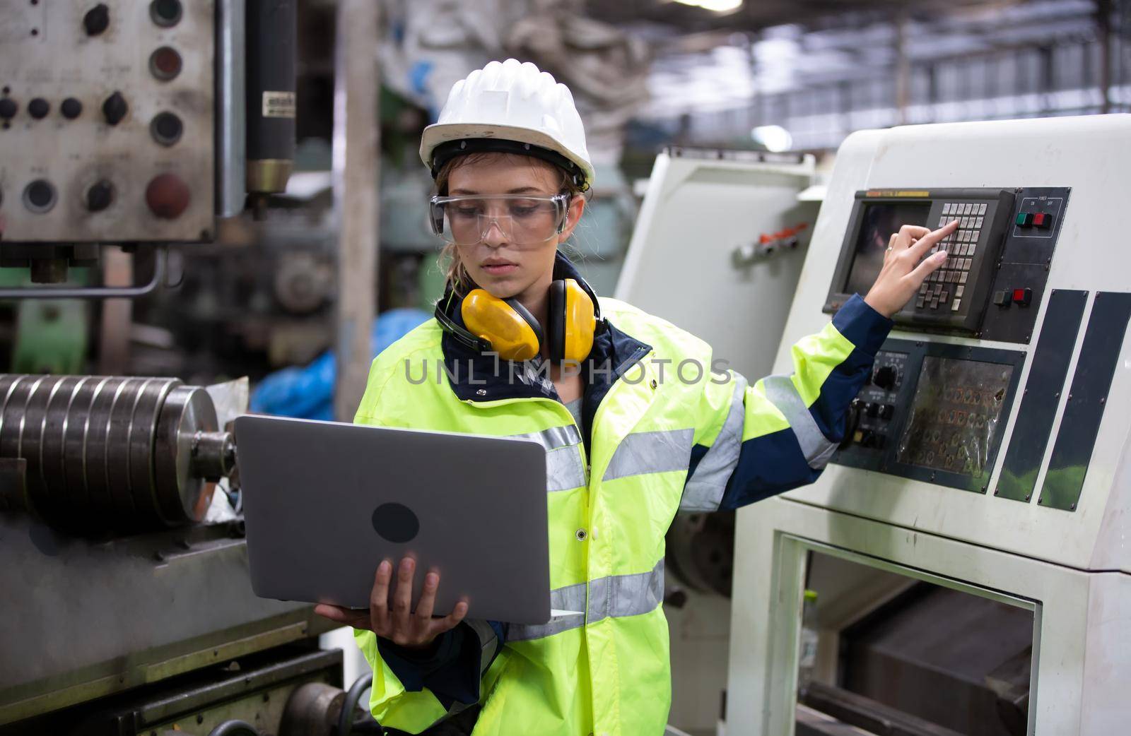 Female technician worker in uniform working on laptop with machine in manufacturing.	
