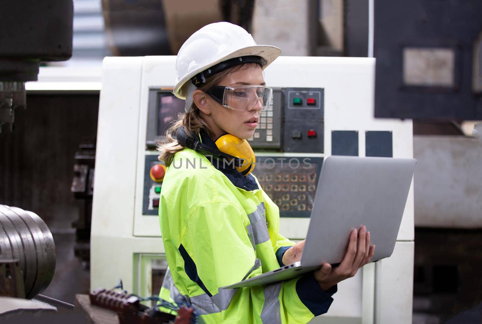 Female technician worker in uniform working on laptop with machine in manufacturing.