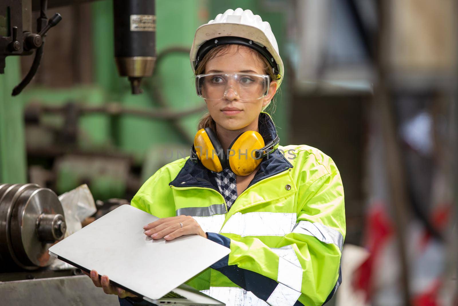 Female technician worker in uniform working on laptop with machine in manufacturing.