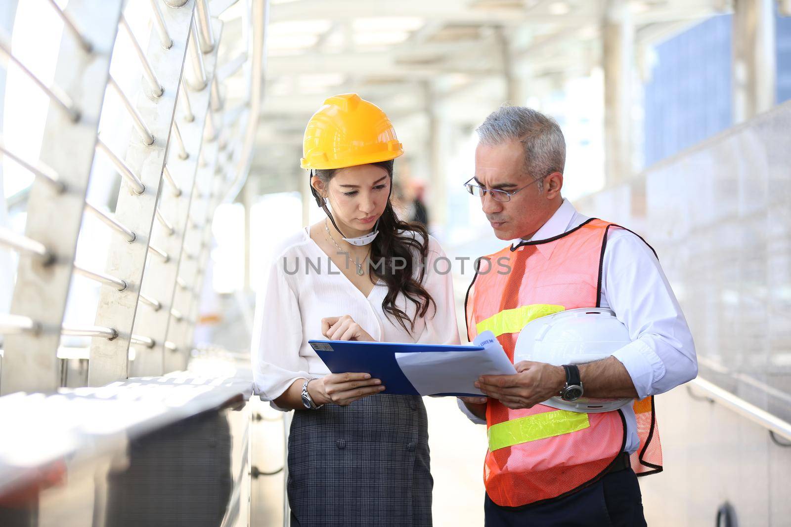 Female industrial engineer wearing a white helmet while standing in a construction site with businessman talking on working plan, Engineer and architects at construction site concept by chuanchai