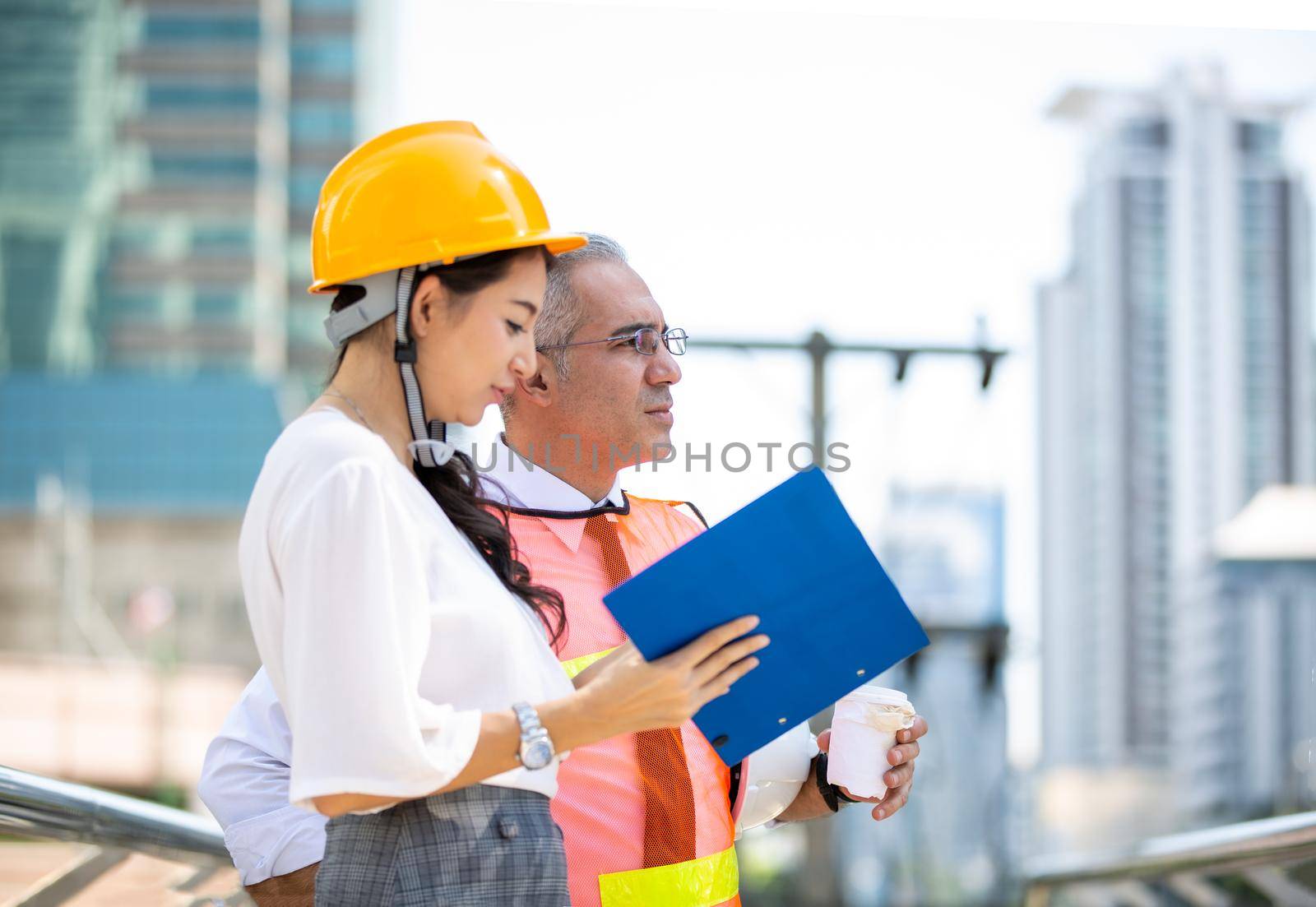 Female industrial engineer wearing a white helmet while standing in a construction site with businessman talking on working plan, Engineer and architects at construction site concept
