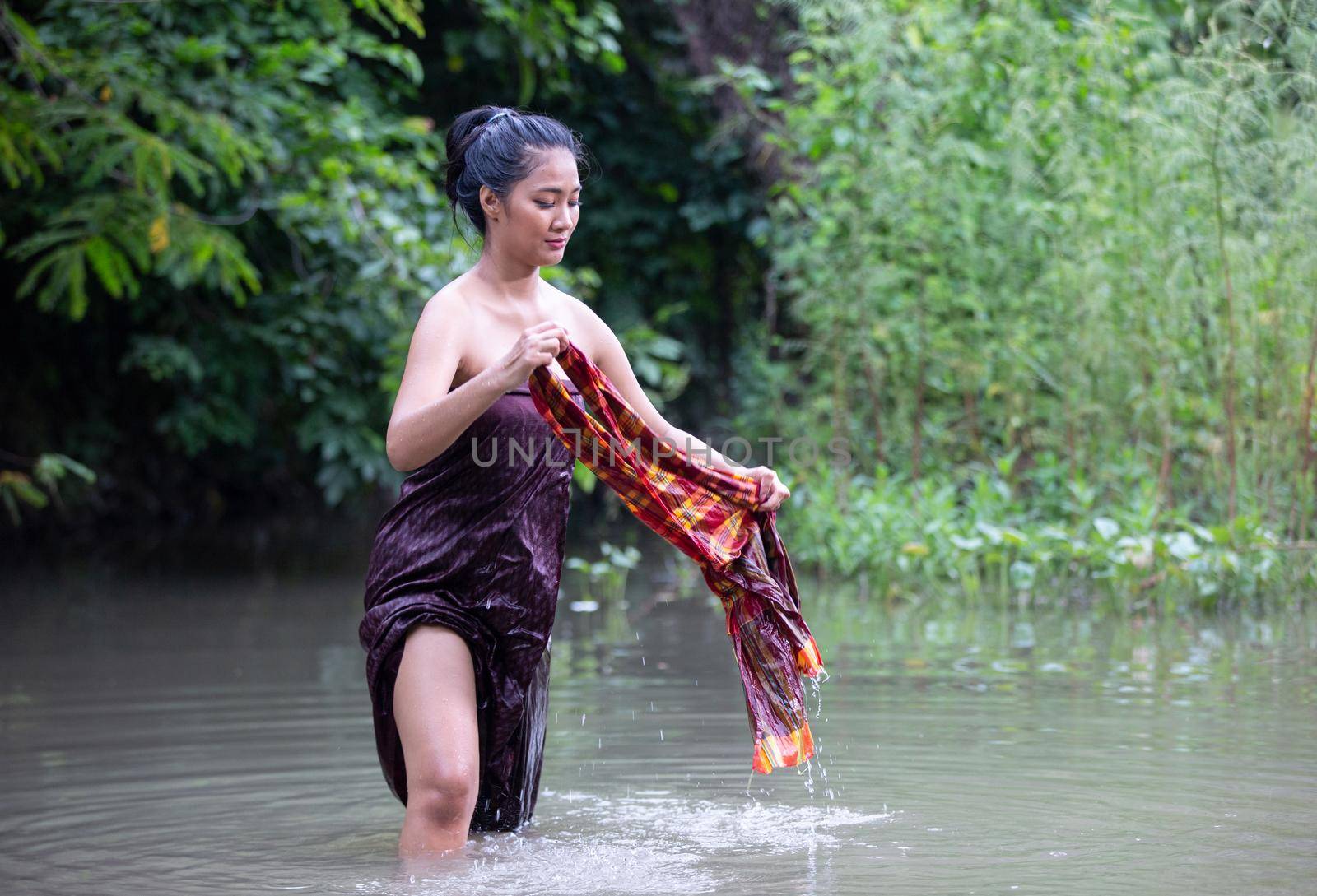 Beautiful Asian women are bathing in the river. Asia girl in Thailand. Asian girl take a shower outdoor from a traditional bamboo chute,countryside Thailand.