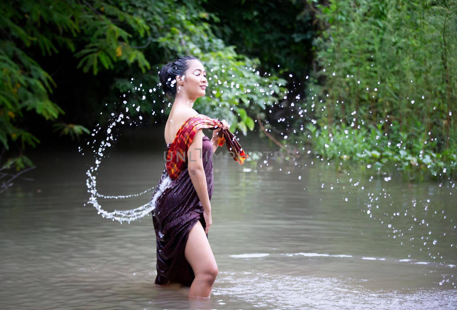 Beautiful Asian women are bathing in the river. Asia girl in Thailand. Asian girl take a shower outdoor from a traditional bamboo chute,countryside Thailand. by chuanchai