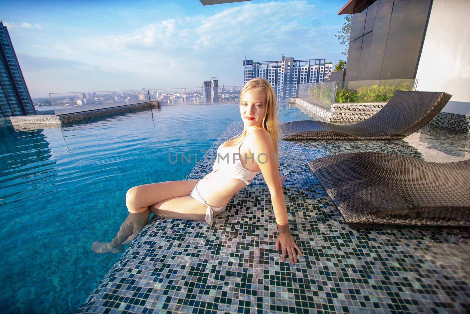 Young woman enjoying a sun, Slim young girl model in white bikini  by the pool.