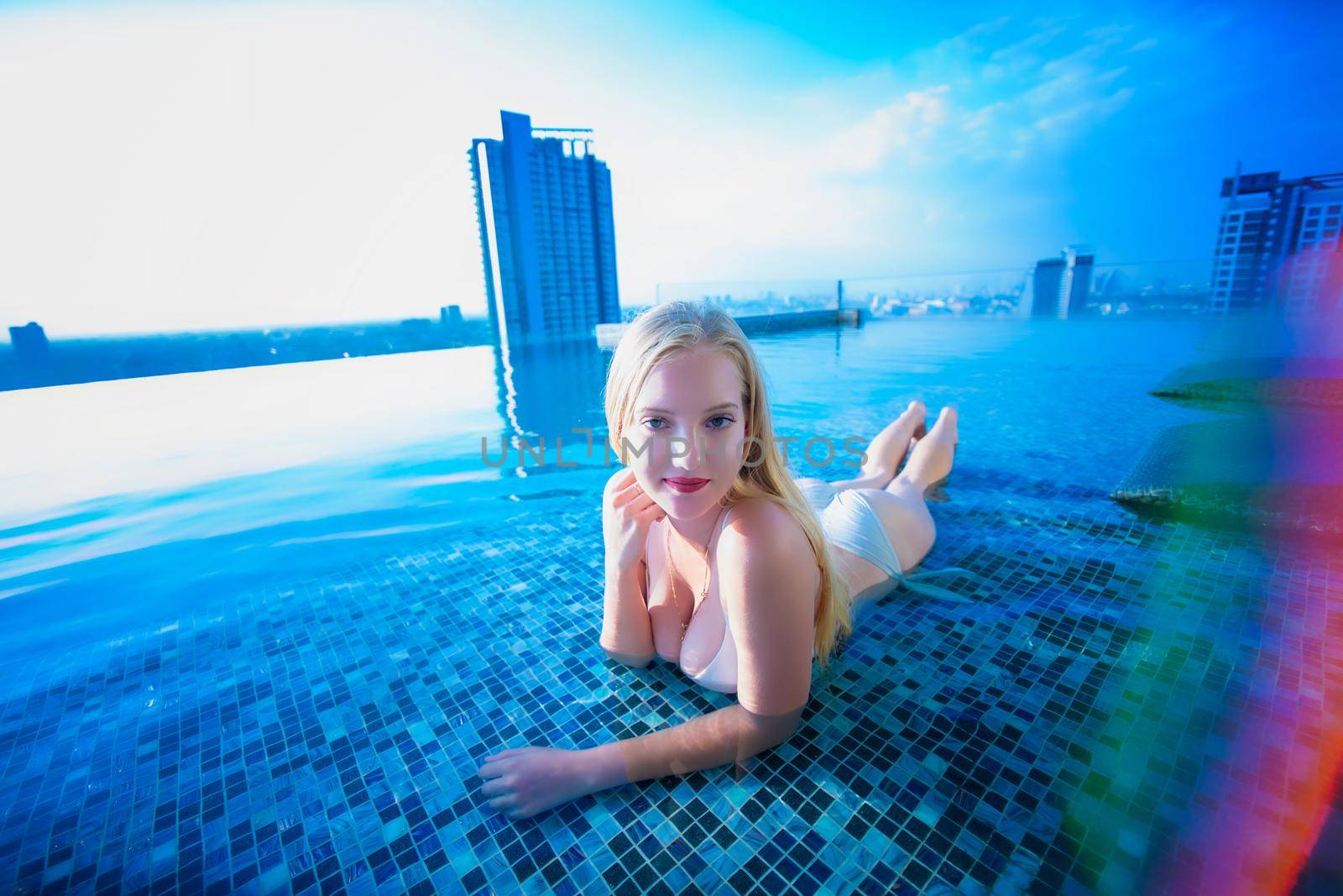 Young woman enjoying a sun, Slim young girl model in white bikini  by the pool.