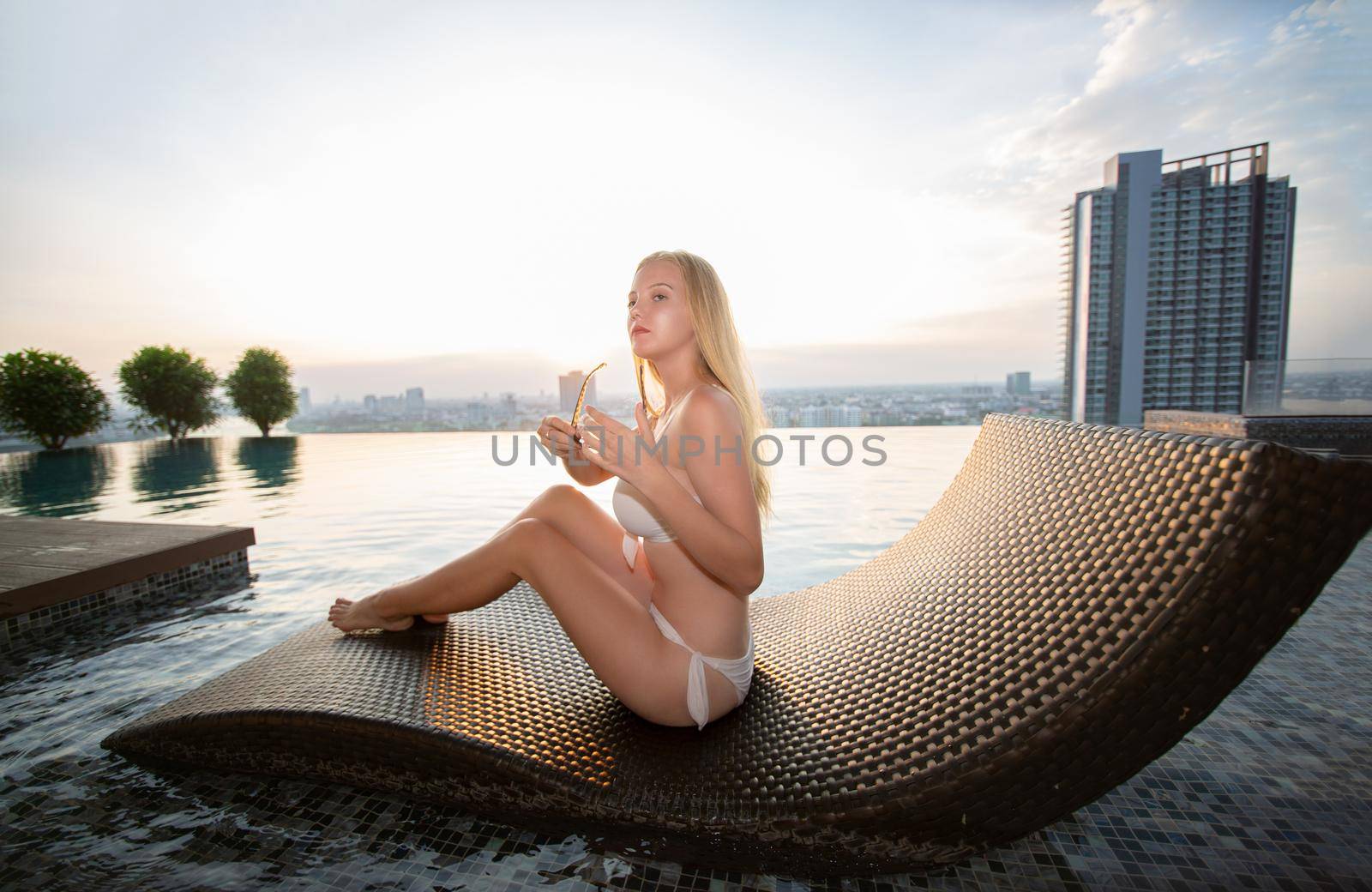 Young woman enjoying a sun, Slim young girl model in white bikini  by the pool.