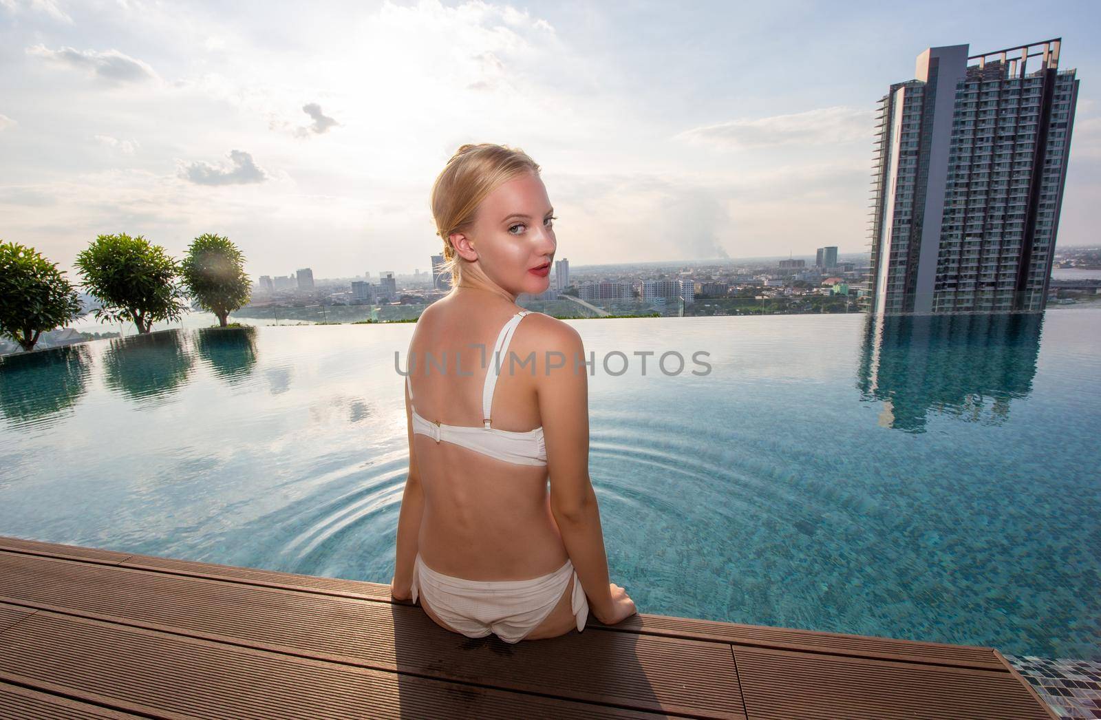 Young woman enjoying a sun, Slim young girl model in white bikini  by the pool.