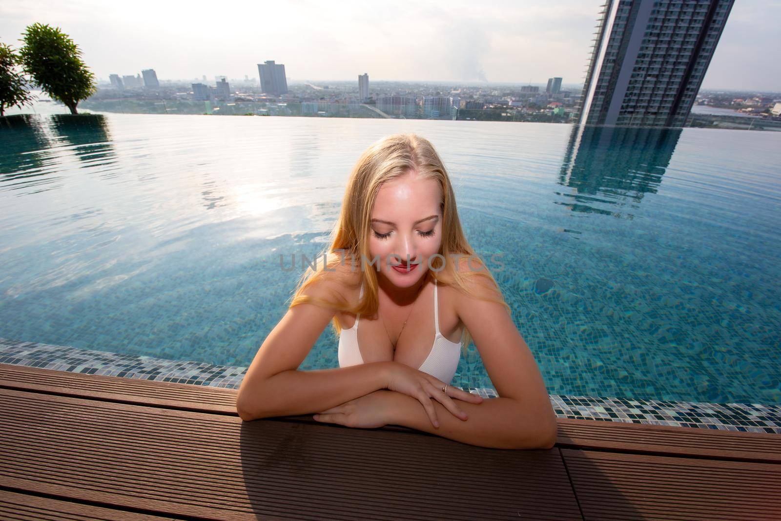 Young woman enjoying a sun, Slim young girl model in white bikini  by the pool.