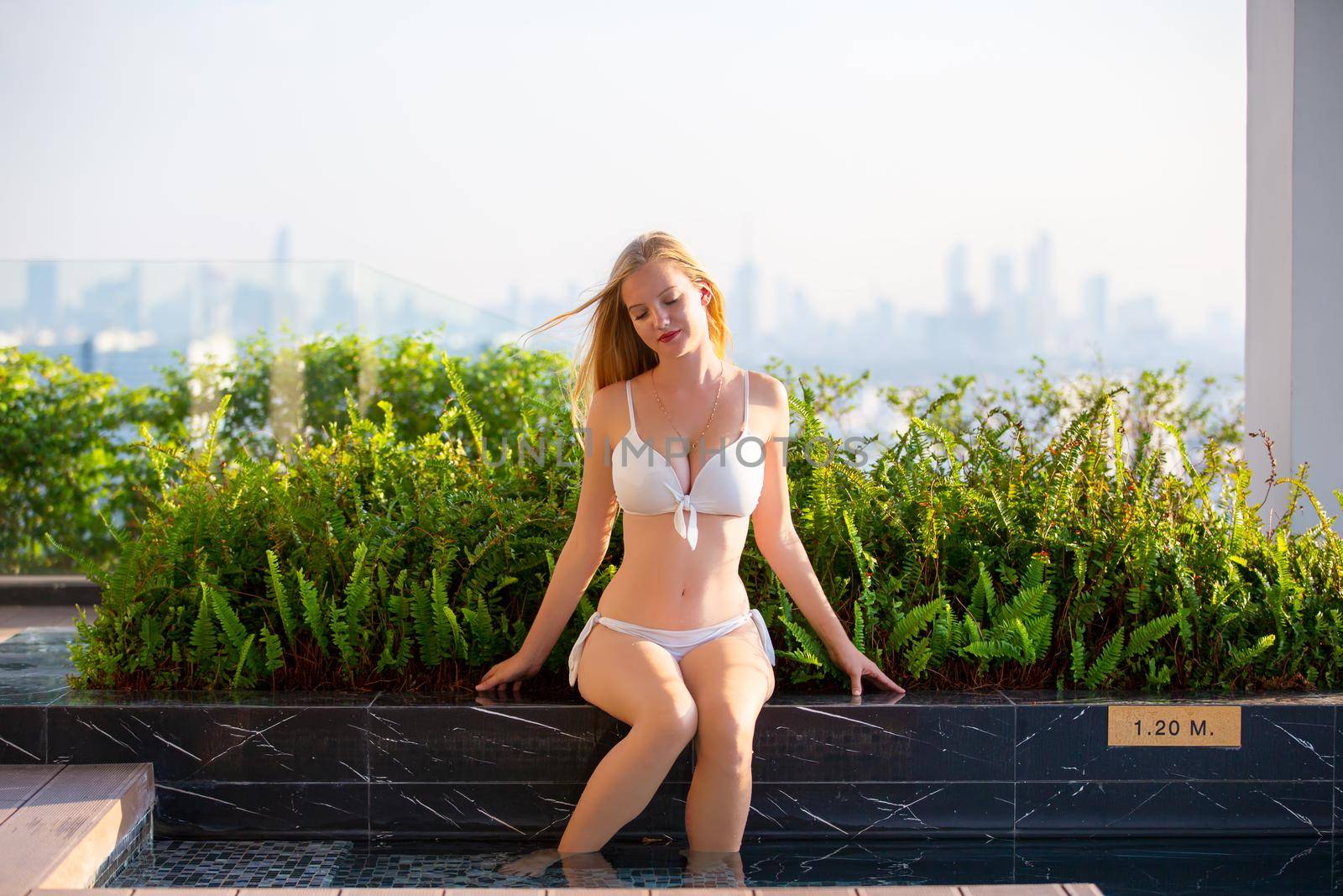 Young woman enjoying a sun, Slim young girl model in white bikini  by the pool.