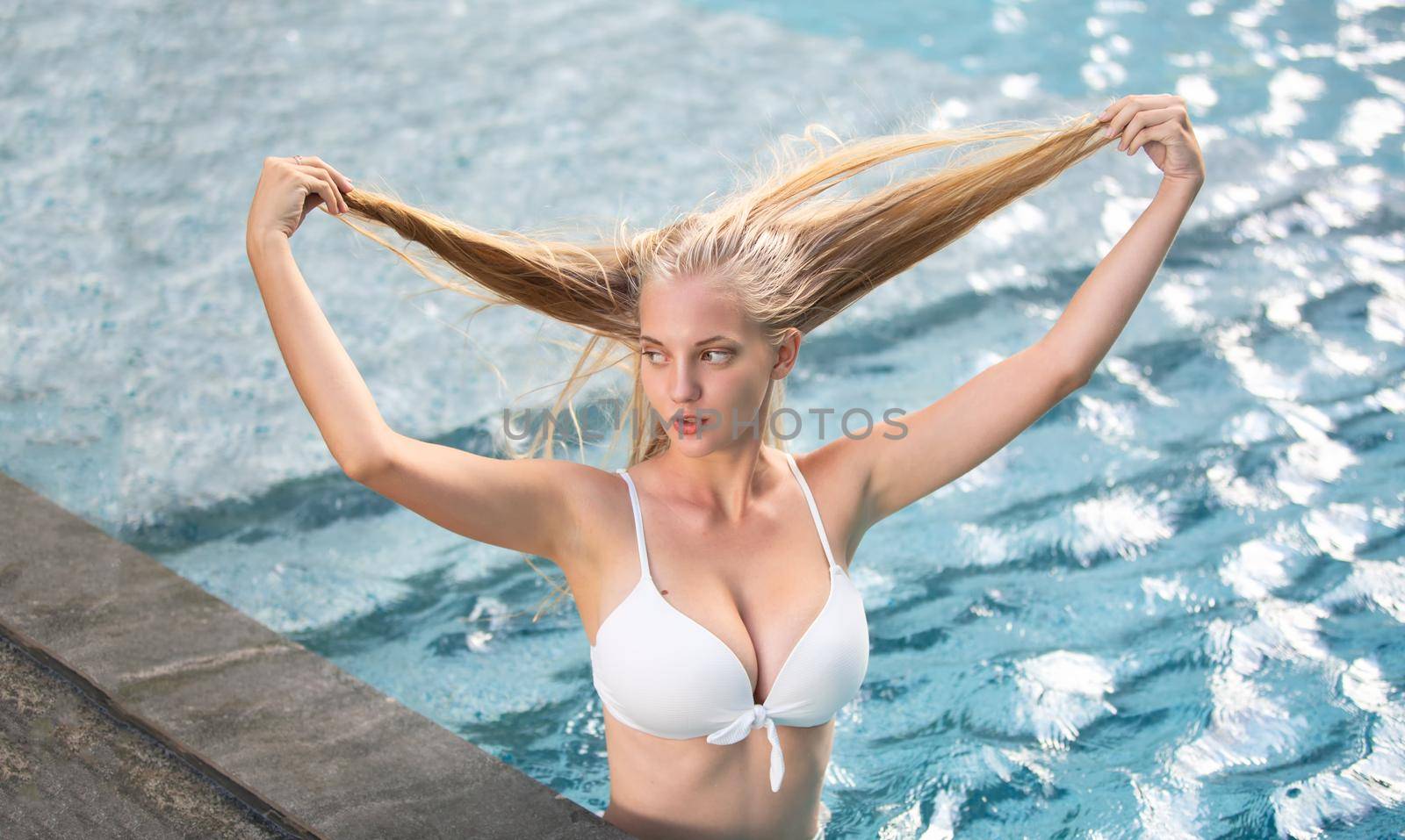 Young woman enjoying a sun, Slim young girl model in white bikini by the pool.