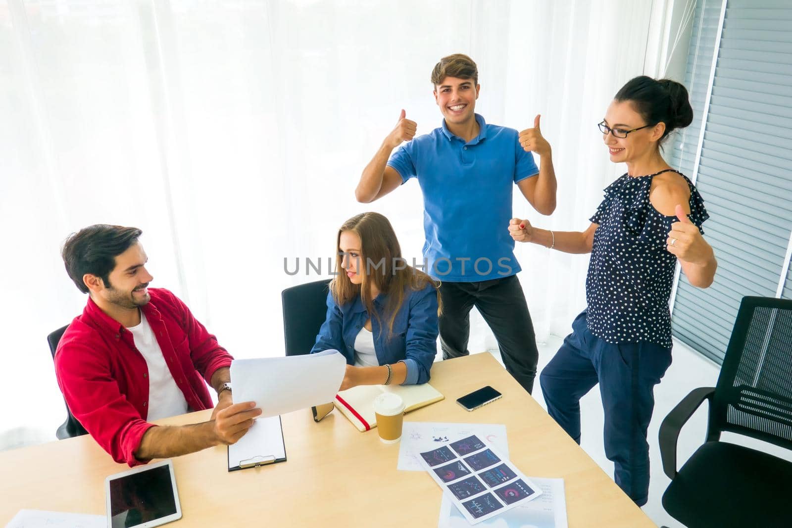 Smiling group of diverse businesspeople going over paperwork together and working on a laptop at a table in an office by chuanchai