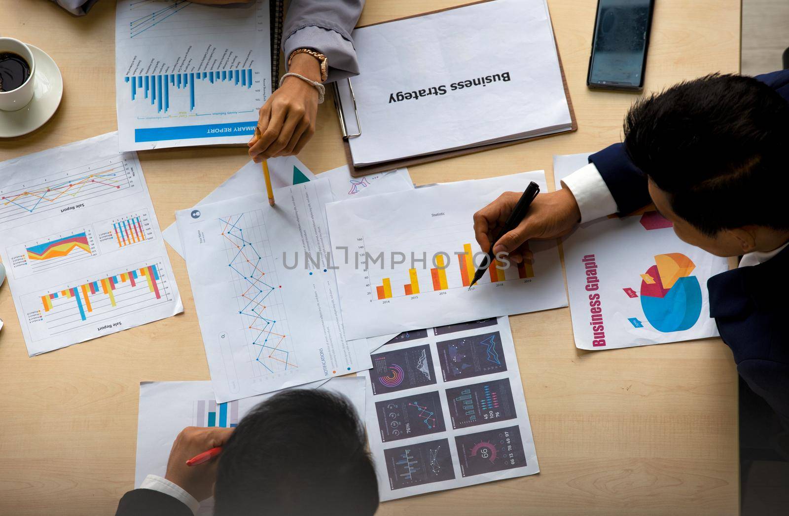 young business team working together at office. Manager pointing at a chart and explaining the analysis about business strategies. Top view shot of business hand shake