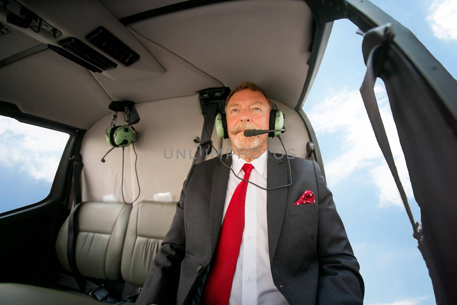 Business people traveling by helicopter , Shot of a mature businessman using a headset while traveling in a helicopter by chuanchai