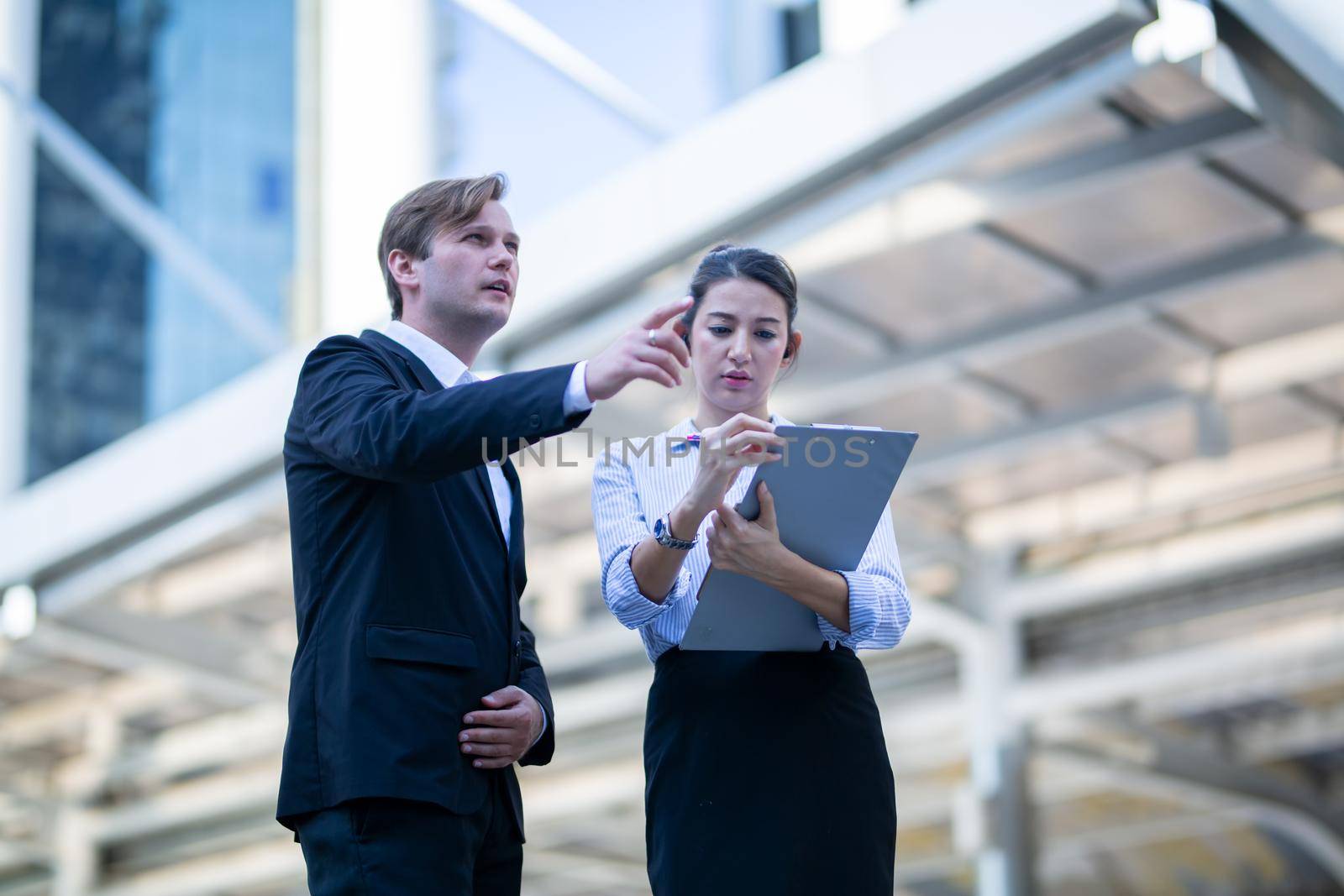 Businessman and women sitting on step outdoor looking on laptop against building