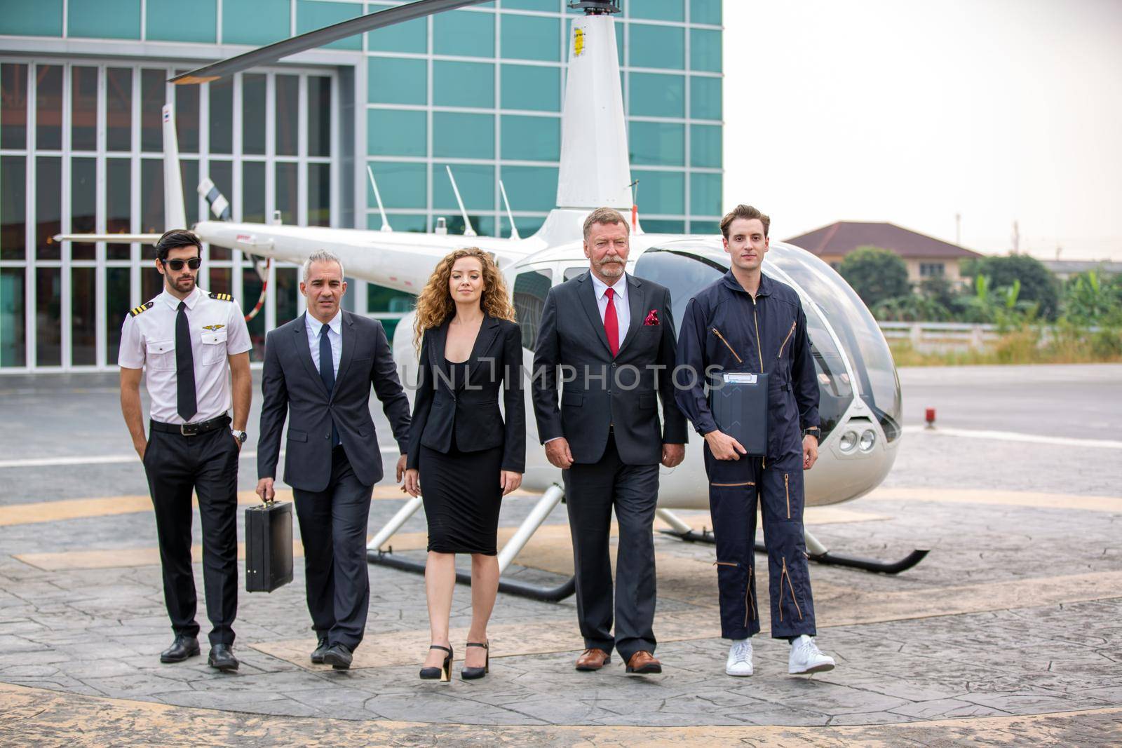 Close up of a male helicopter pilot wear sun glass and business people or executive CEO standing against helicopter at aircraft landing point in airport on a bright sunny day. by chuanchai