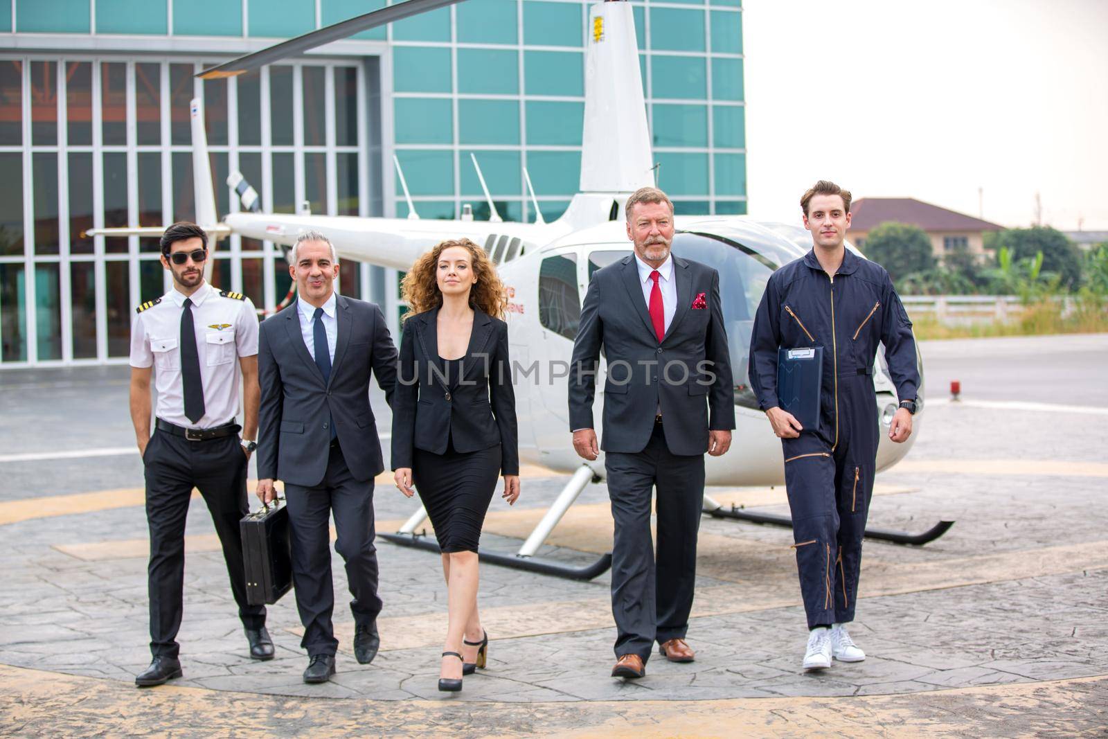 Close up of a male helicopter pilot wear sun glass and business people or executive CEO standing against helicopter at aircraft landing point in airport on a bright sunny day. by chuanchai
