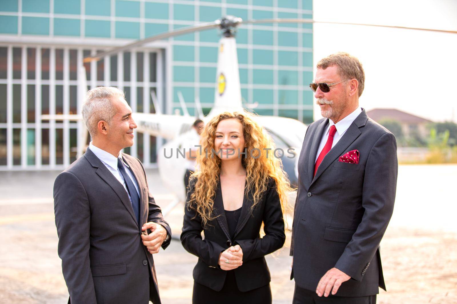 Close up of a male helicopter pilot wear sun glass and business people or executive CEO standing against helicopter at aircraft landing point in airport on a bright sunny day. by chuanchai