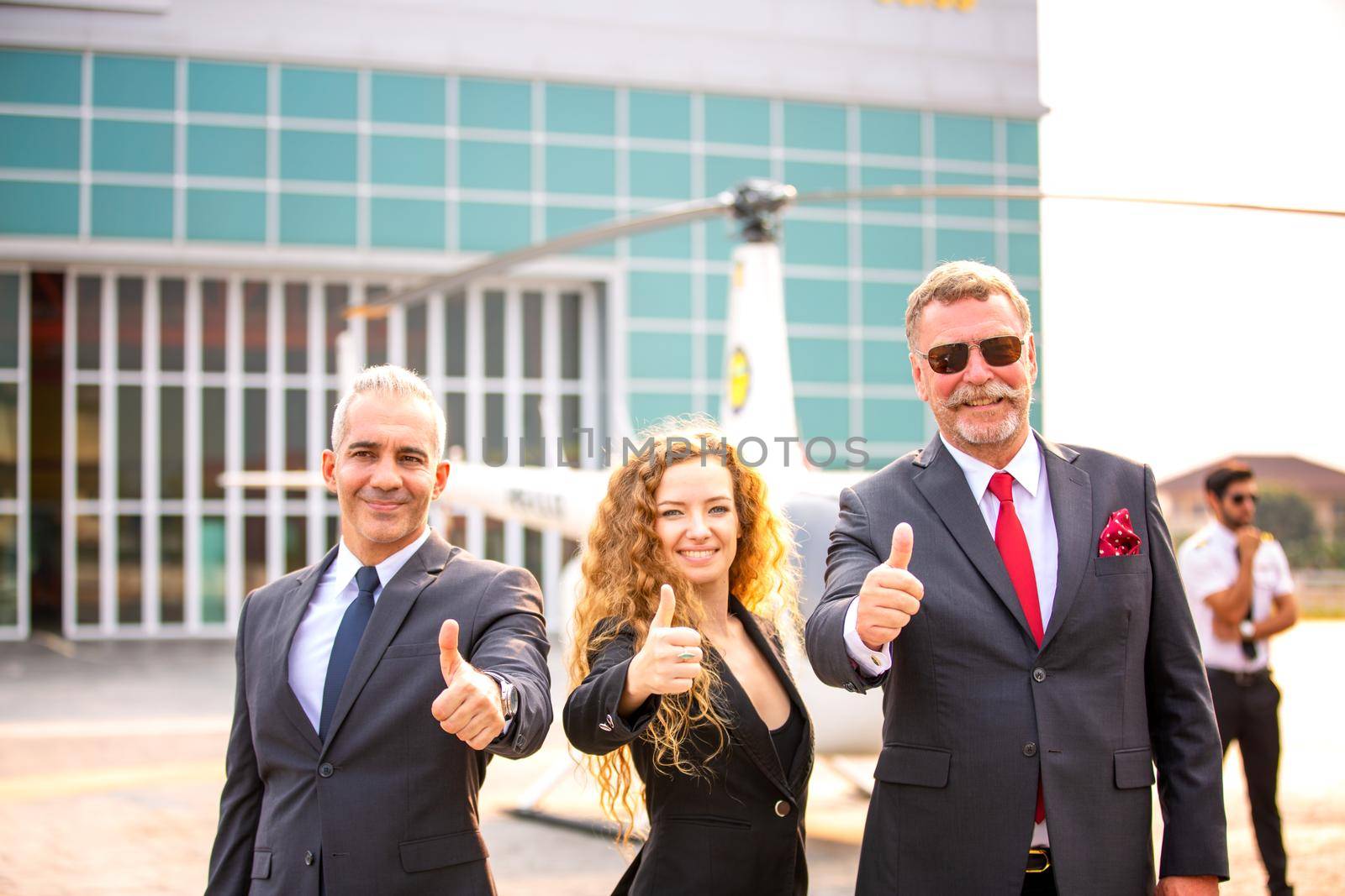 Close up of a male helicopter pilot wear sun glass and business people or executive CEO standing against helicopter at aircraft landing point in airport on a bright sunny day. by chuanchai