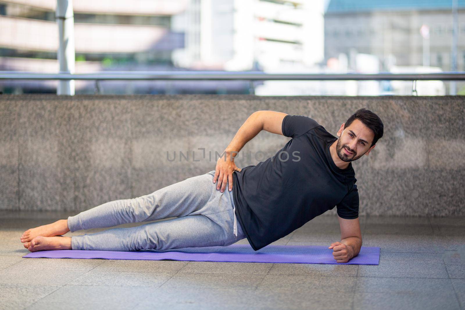 Young attractive smiling man practicing yoga pose, working out, wearing sportswear pants, full length, outdoor.