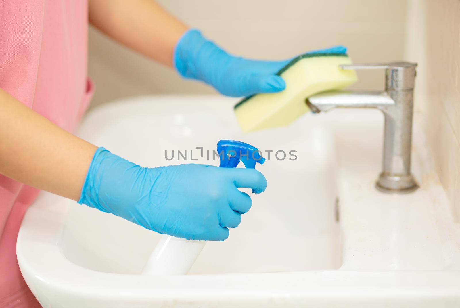 Close-up women hand in a blue rubber glove and cleaning sponge in the picture, removes and washes bathroom sink and mirror by chuanchai