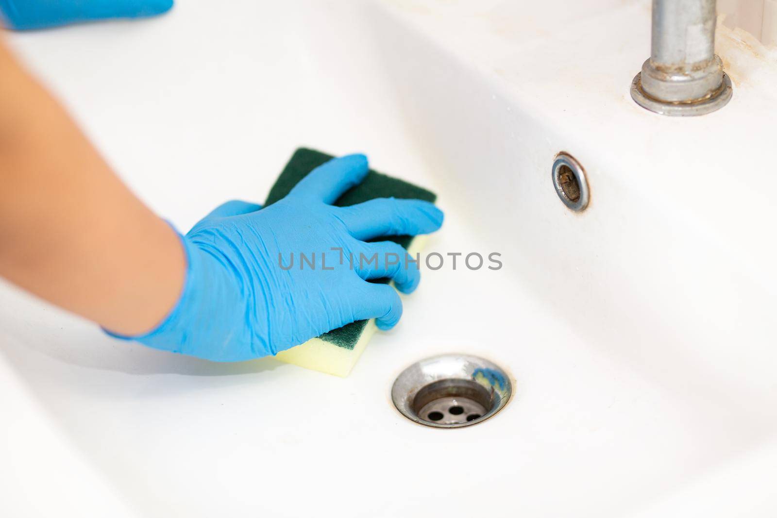 Close-up women hand in a blue rubber glove and cleaning sponge in the picture, removes and washes bathroom sink and mirror. by chuanchai
