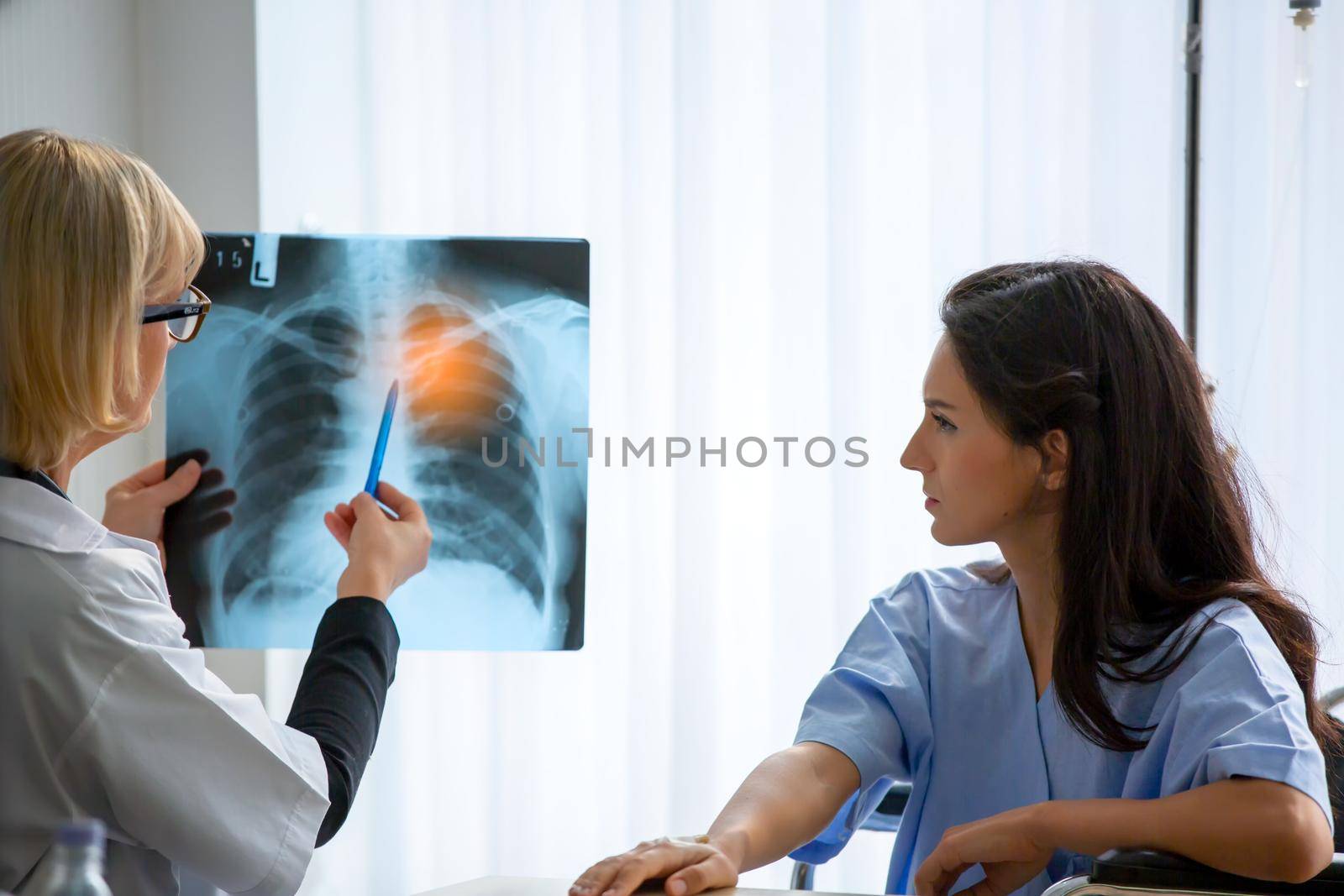 Doctor explaining lungs x-ray to women patient in clinic or Doctor in the office examining an x-ray and discussing with a patient by chuanchai
