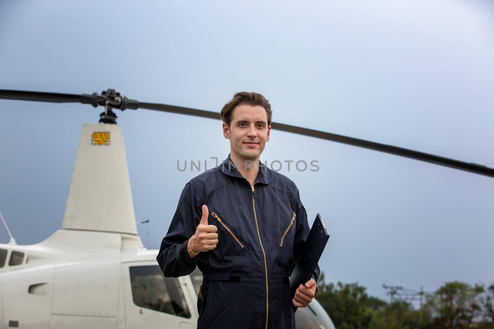 Commercial man pilot in technician suit standing in front of helicopter after check and maintenance engine	