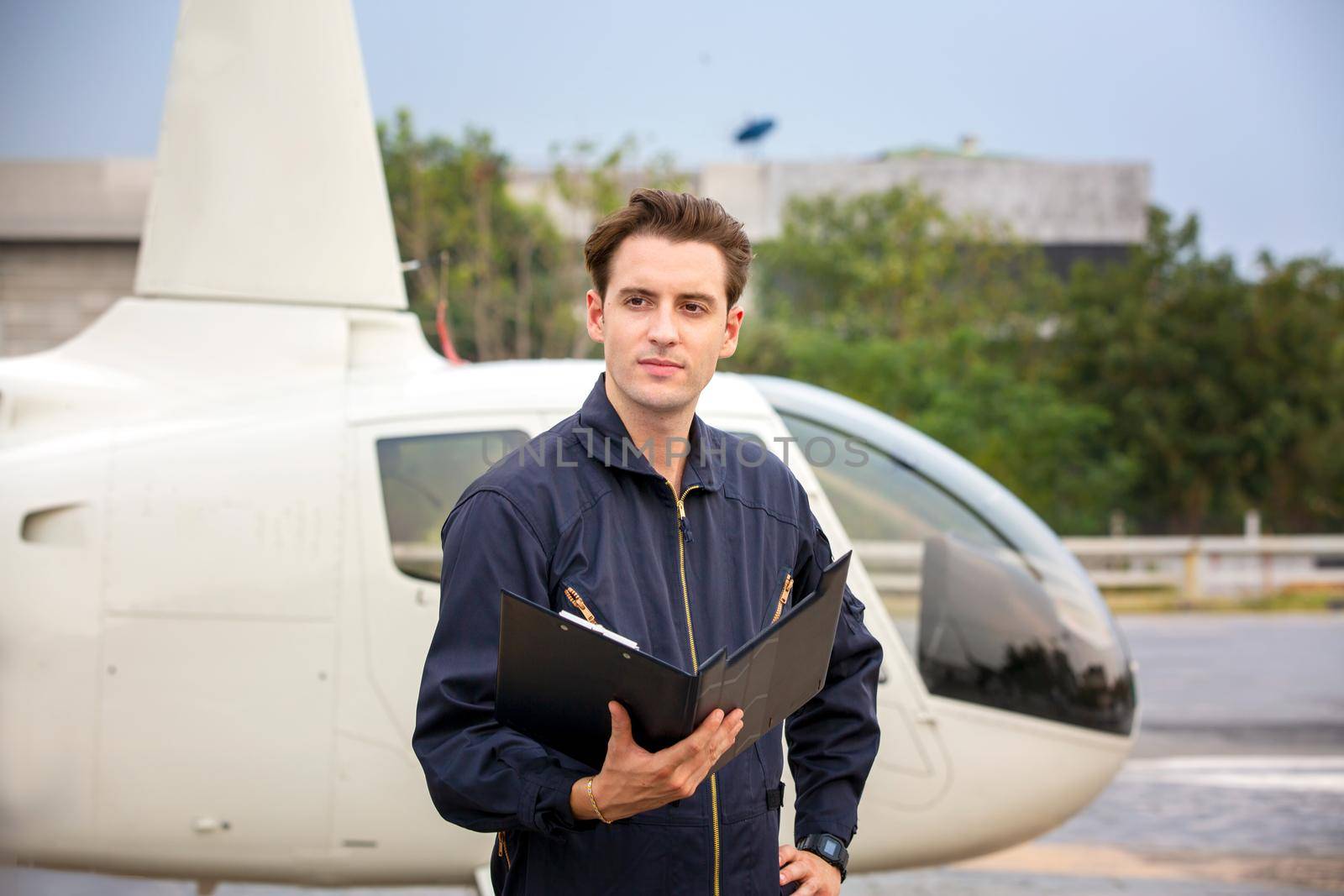 Commercial man pilot in technician suit standing in front of helicopter after check and maintenance engine	