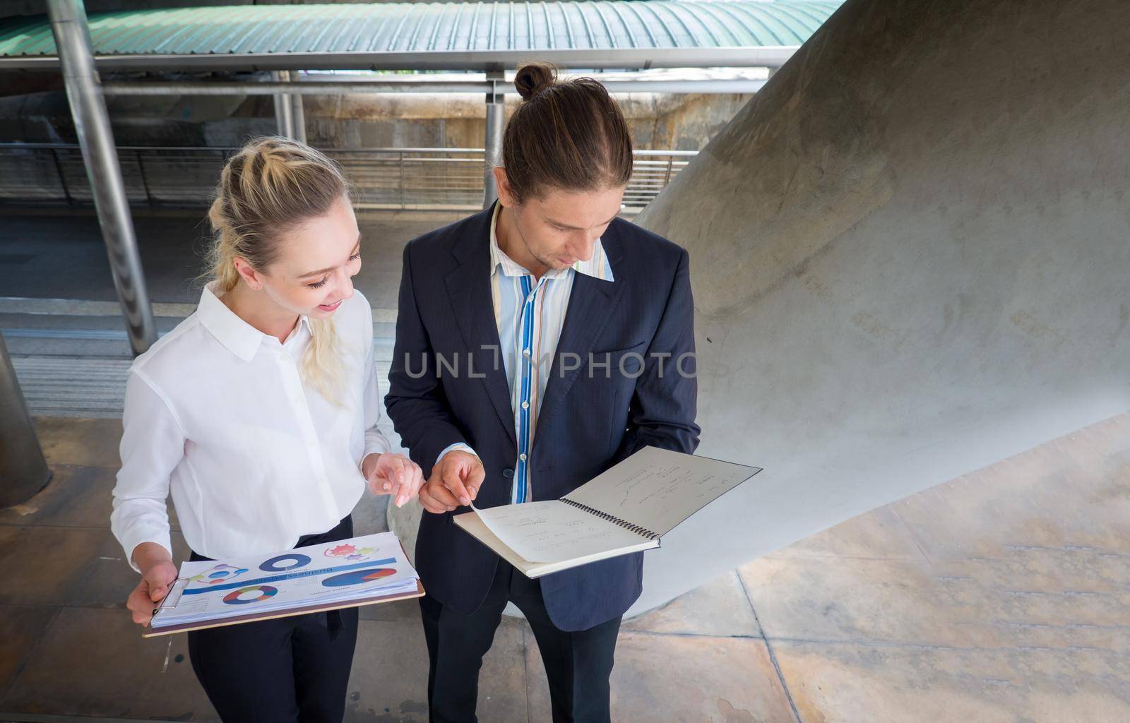 Businessman and businesswoman discussing work while walking outside office by chuanchai