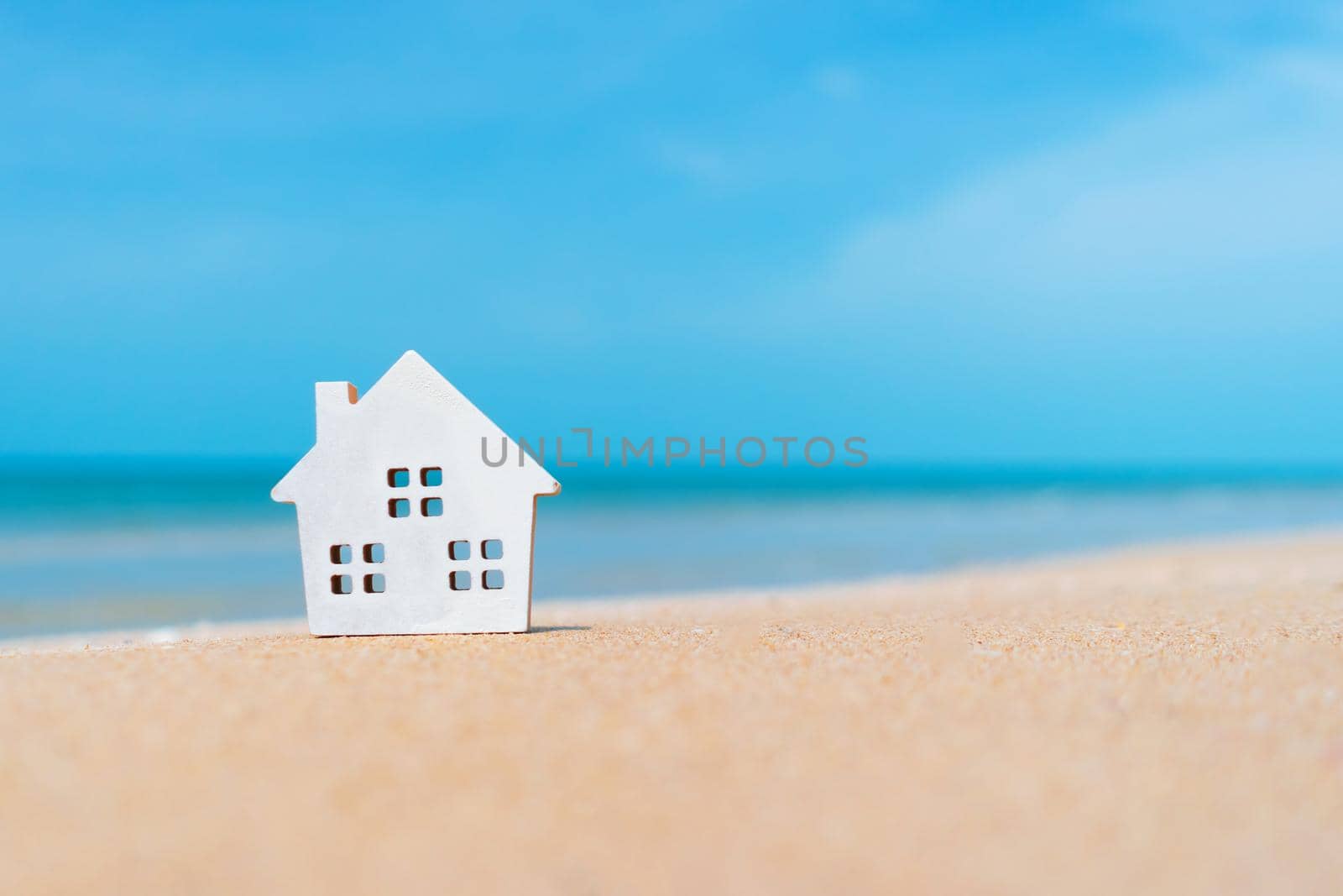 Closed up tiny home models on sand with sunlight and beach background.