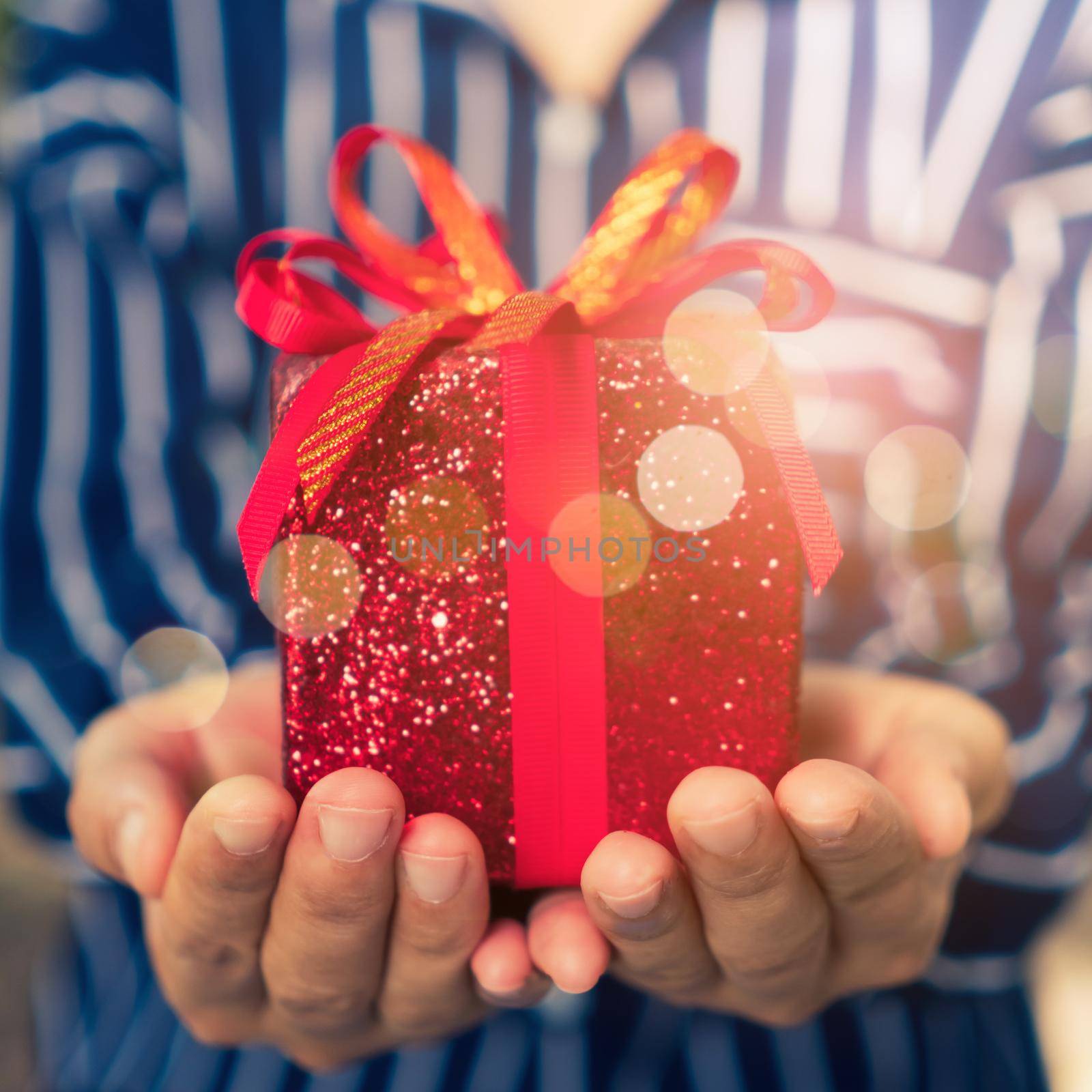 Hand hold gift box to someone on green bokeh nature. Celebration holiday concept.