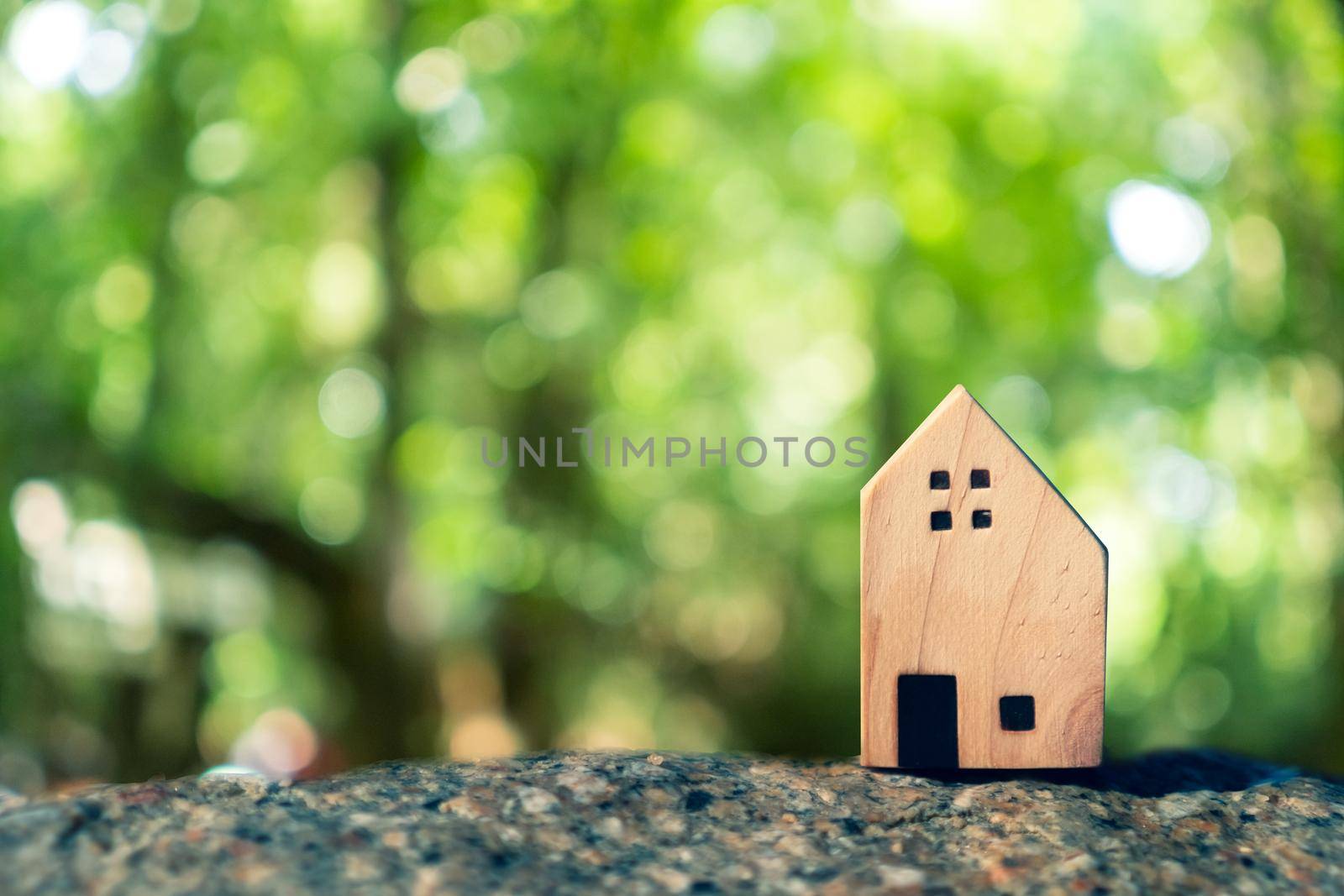 Closed up tiny home model on floor or wood board with sunlight green bokeh background. Deam life have own house property for living or investment concept.