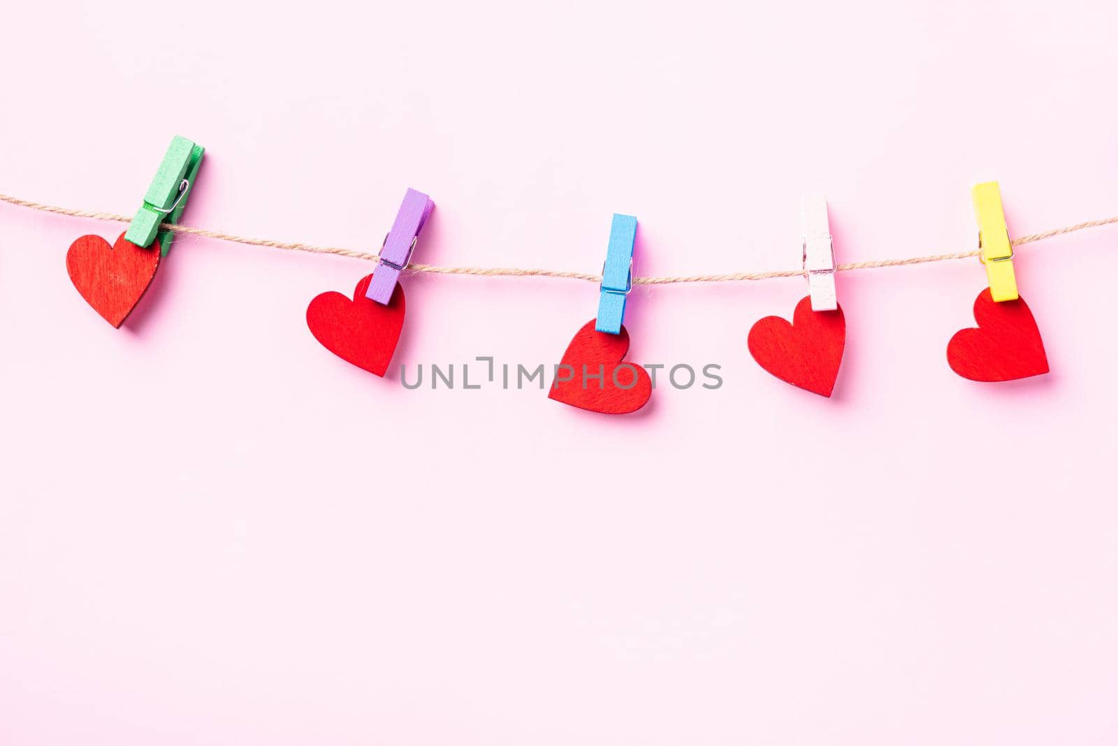 Happy Valentine's day concept. red heart-shaped valentines decoration hanging with wood clips for love on the rope isolated on pink background with copy space